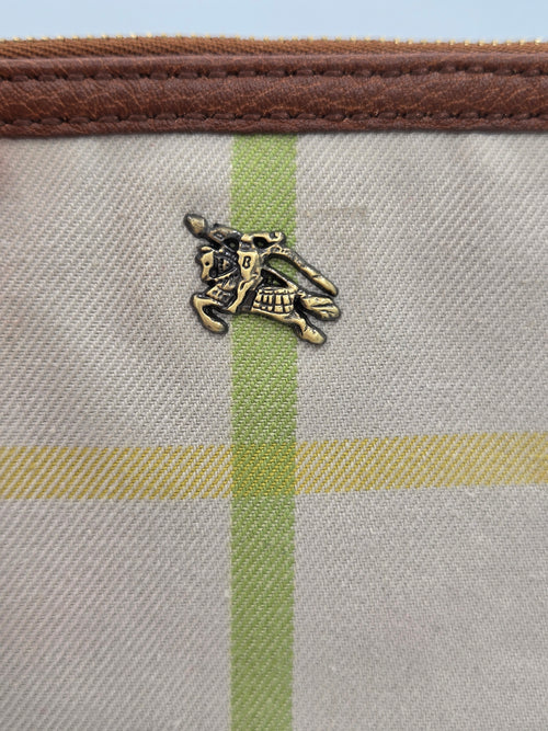Close-up of a canvas pouch featuring a beige and green plaid pattern, a brown leather trim, and a small gold equestrian logo charm.