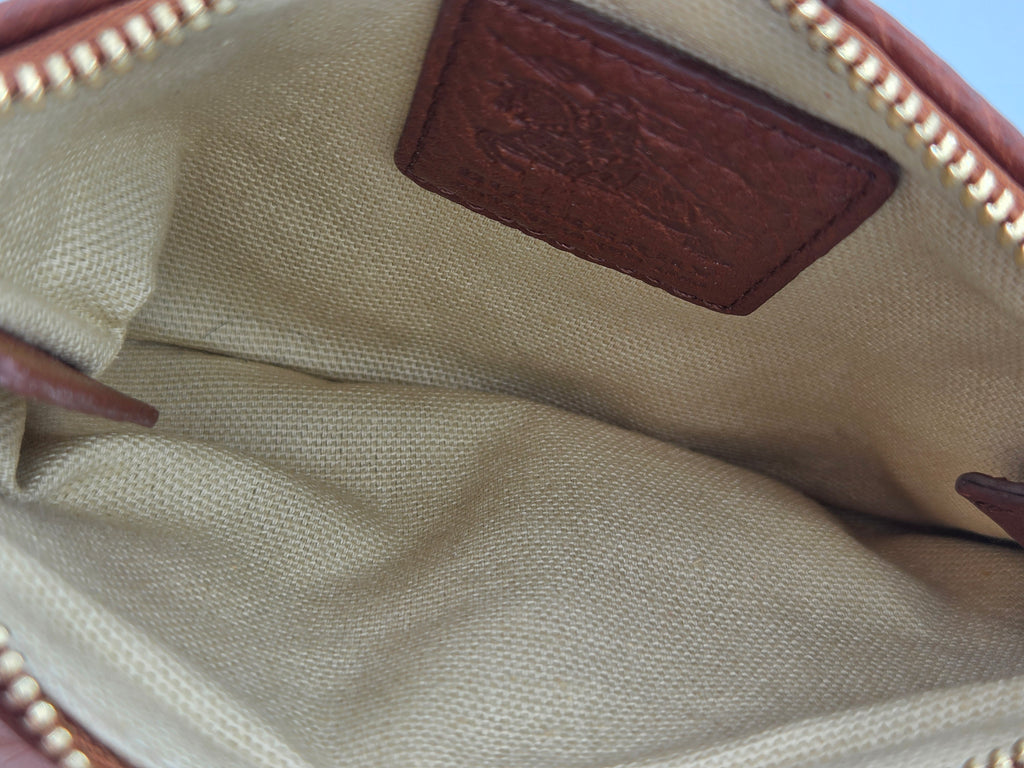Close-up of the interior of a beige canvas bag with a brown leather patch and gold-tone zipper trim.