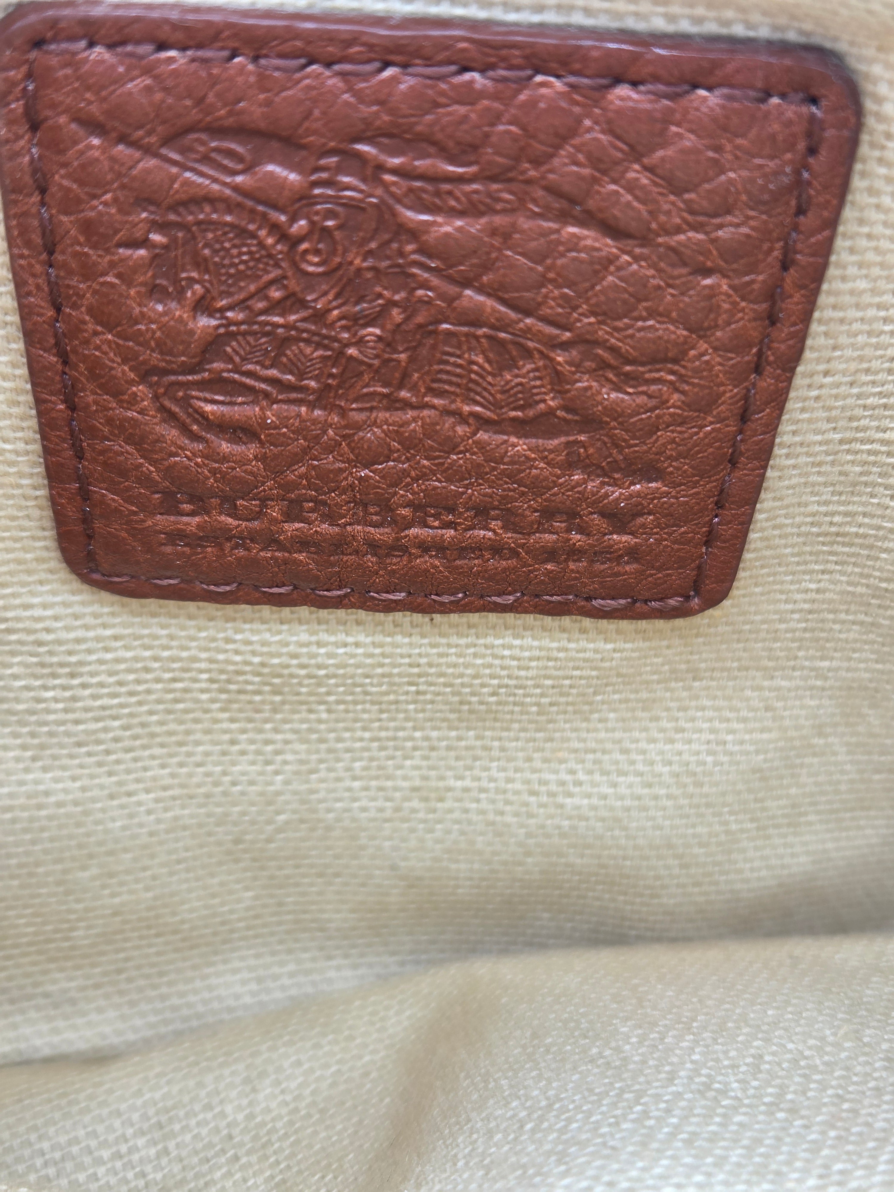 Close-up of a brown textured leather patch with an embossed horse-and-carriage motif, sewn onto a light beige canvas fabric.