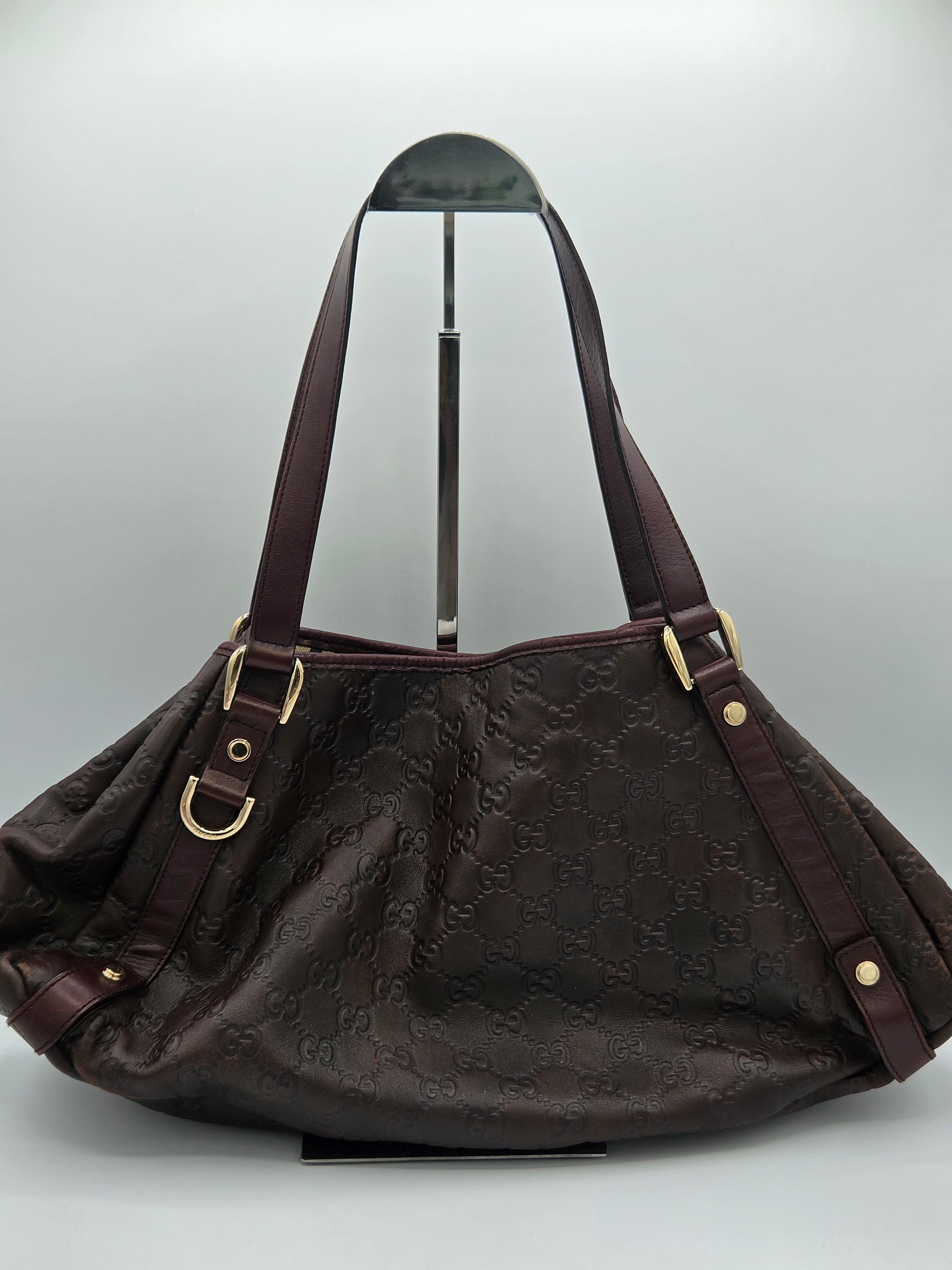 A dark brown Gucci hobo shoulder bag with an embossed GG monogram pattern, displayed on a stand against a light gray background.