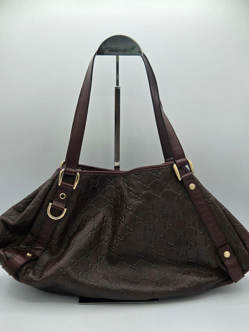 A dark brown Gucci hobo shoulder bag with an embossed GG monogram pattern, displayed on a stand against a light gray background.