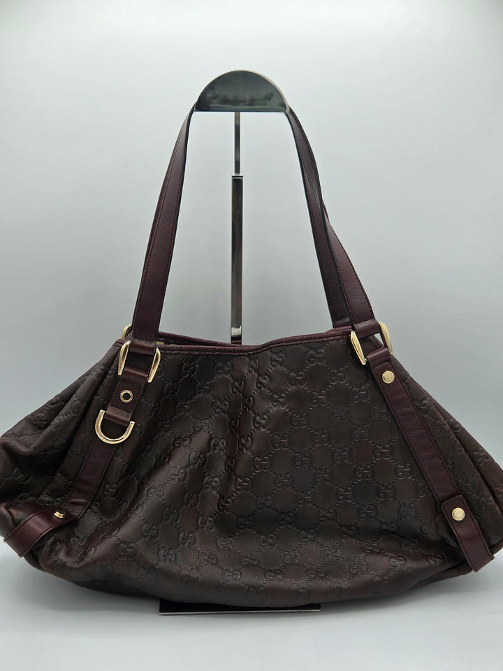 A dark brown Gucci hobo shoulder bag with an embossed GG monogram pattern, displayed on a stand against a light gray background.
