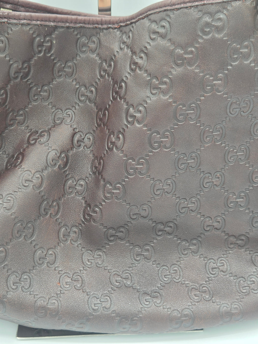 Close-up of a brown leather item featuring an embossed repeating interlocking GG monogram pattern, likely a bag or accessory.