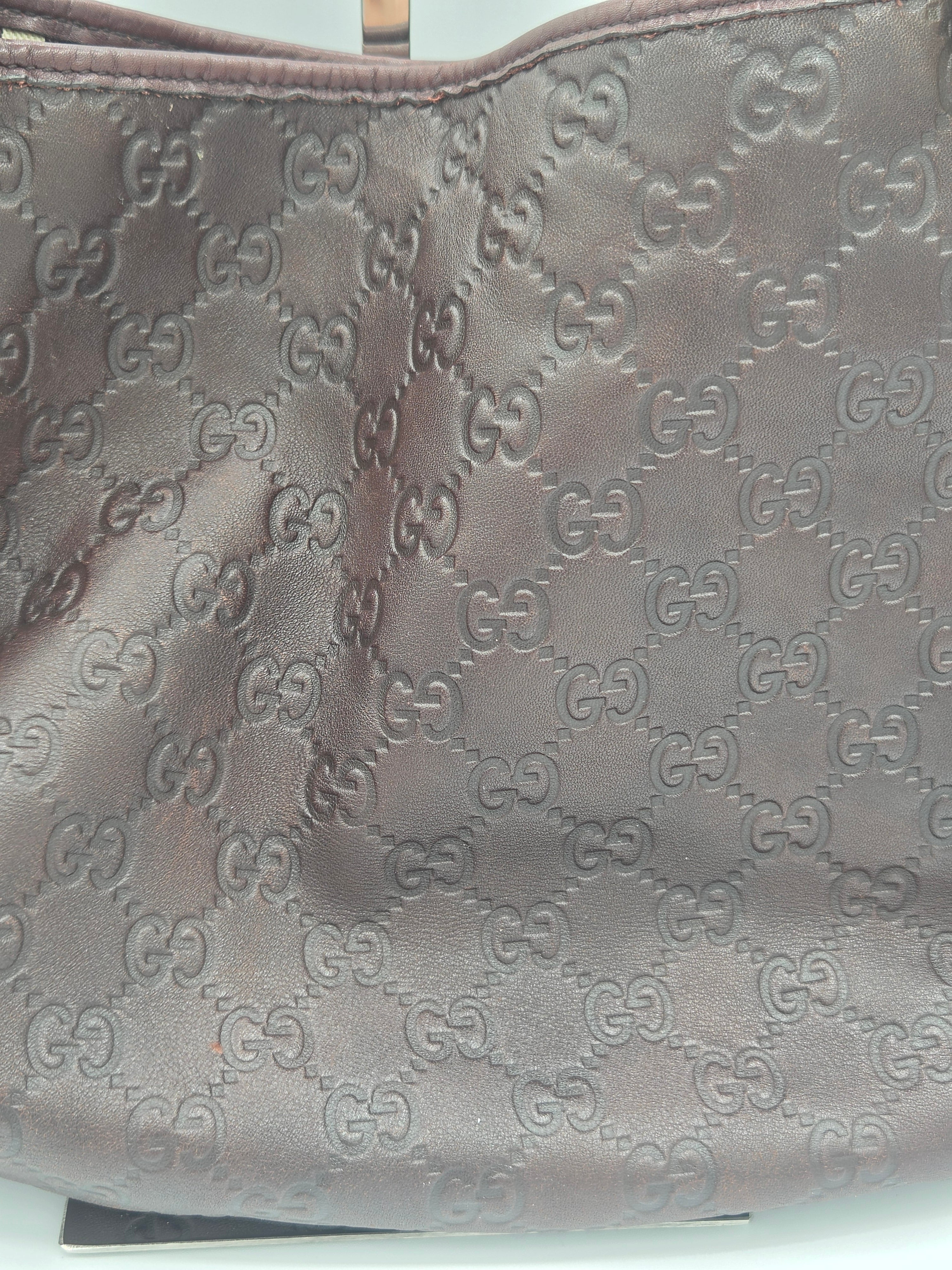 Close-up of a brown leather item featuring an embossed repeating interlocking GG monogram pattern, likely a bag or accessory.