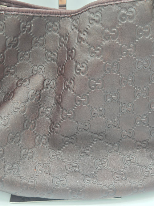 Close-up of a brown leather item featuring an embossed repeating interlocking GG monogram pattern, likely a bag or accessory.