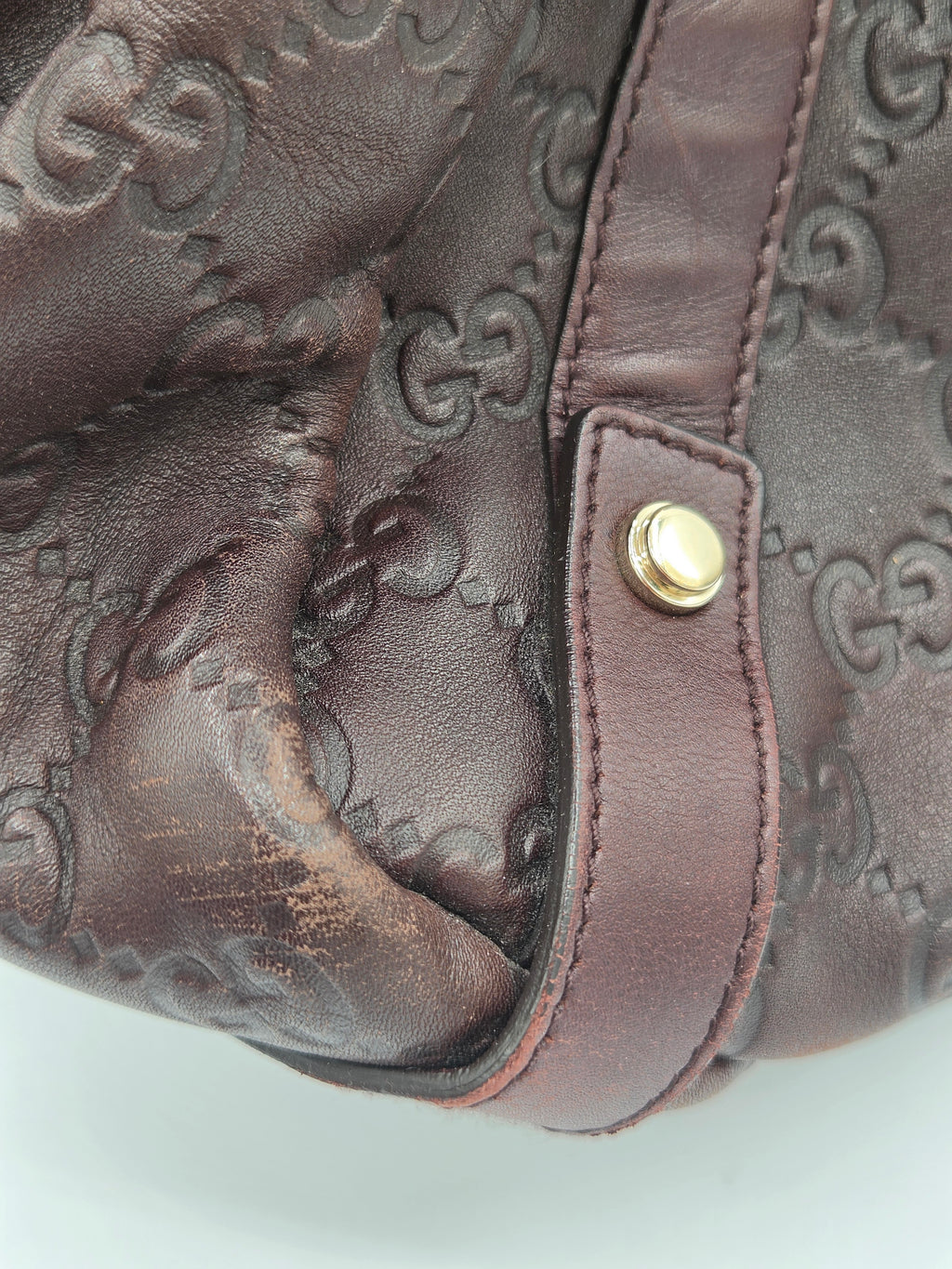 Close-up of a dark brown leather handbag featuring the embossed Gucci GG monogram pattern and a gold-tone metal snap button on a strap.