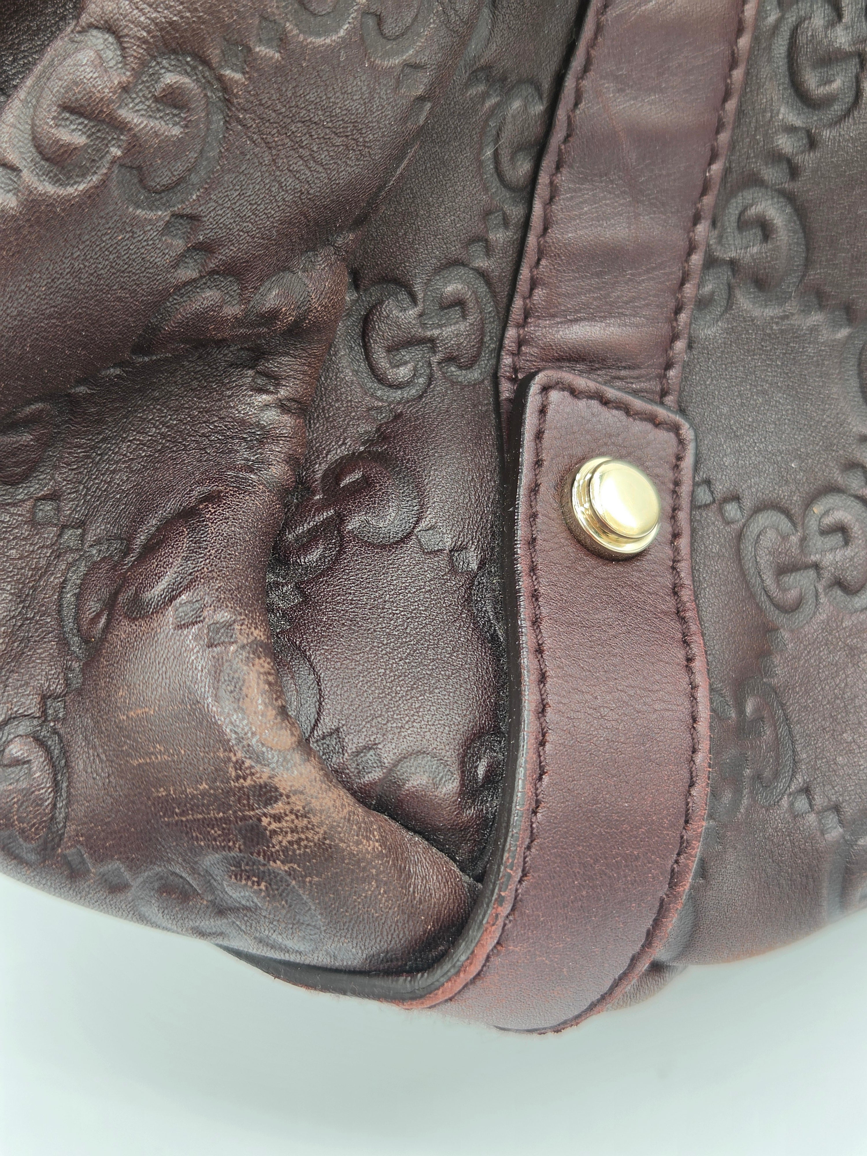 Close-up of a dark brown leather handbag featuring the embossed Gucci GG monogram pattern and a gold-tone metal snap button on a strap.