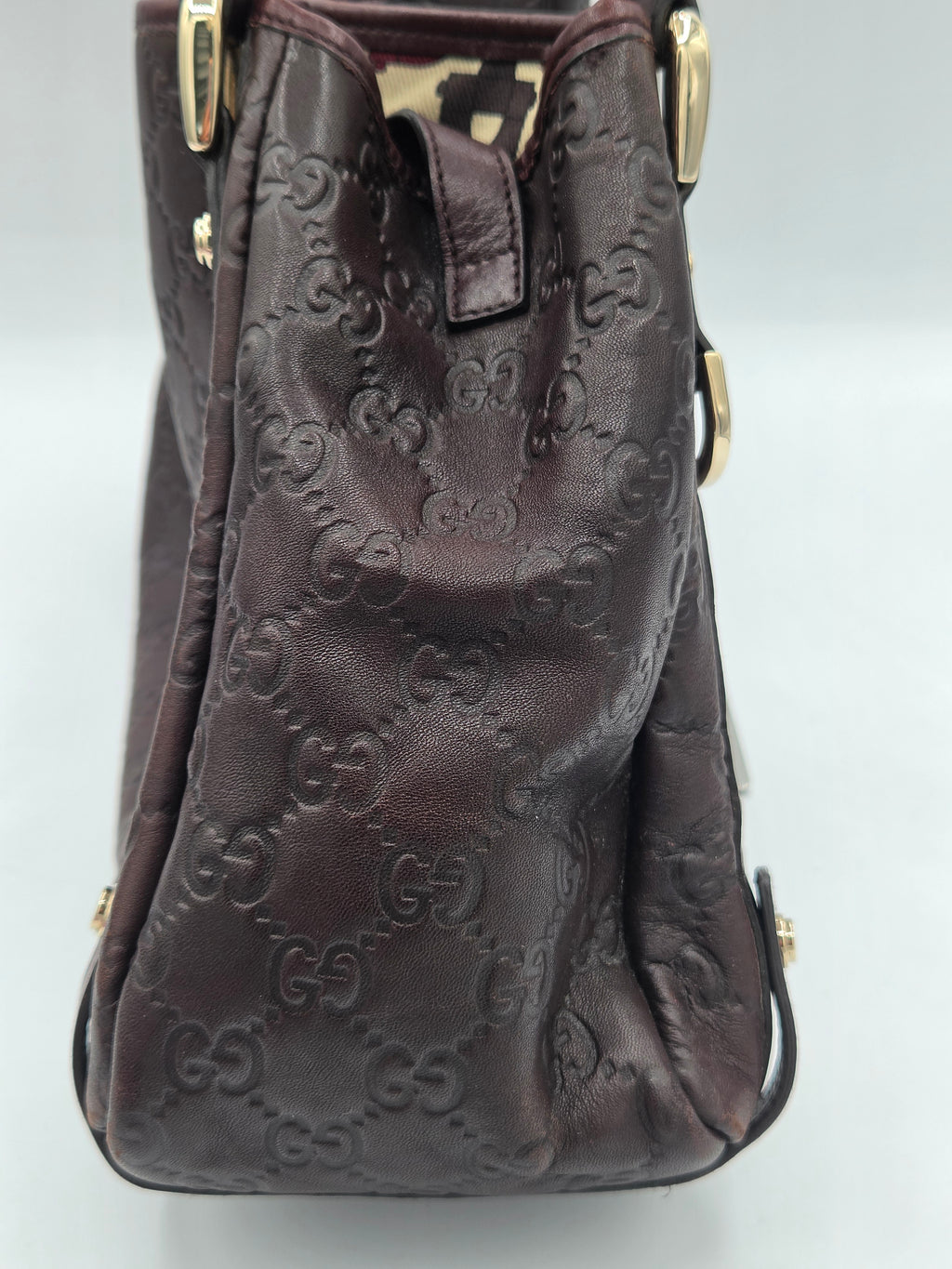 A dark brown leather handbag featuring an embossed monogram pattern, shown from a top-down angle against a light gray background.
