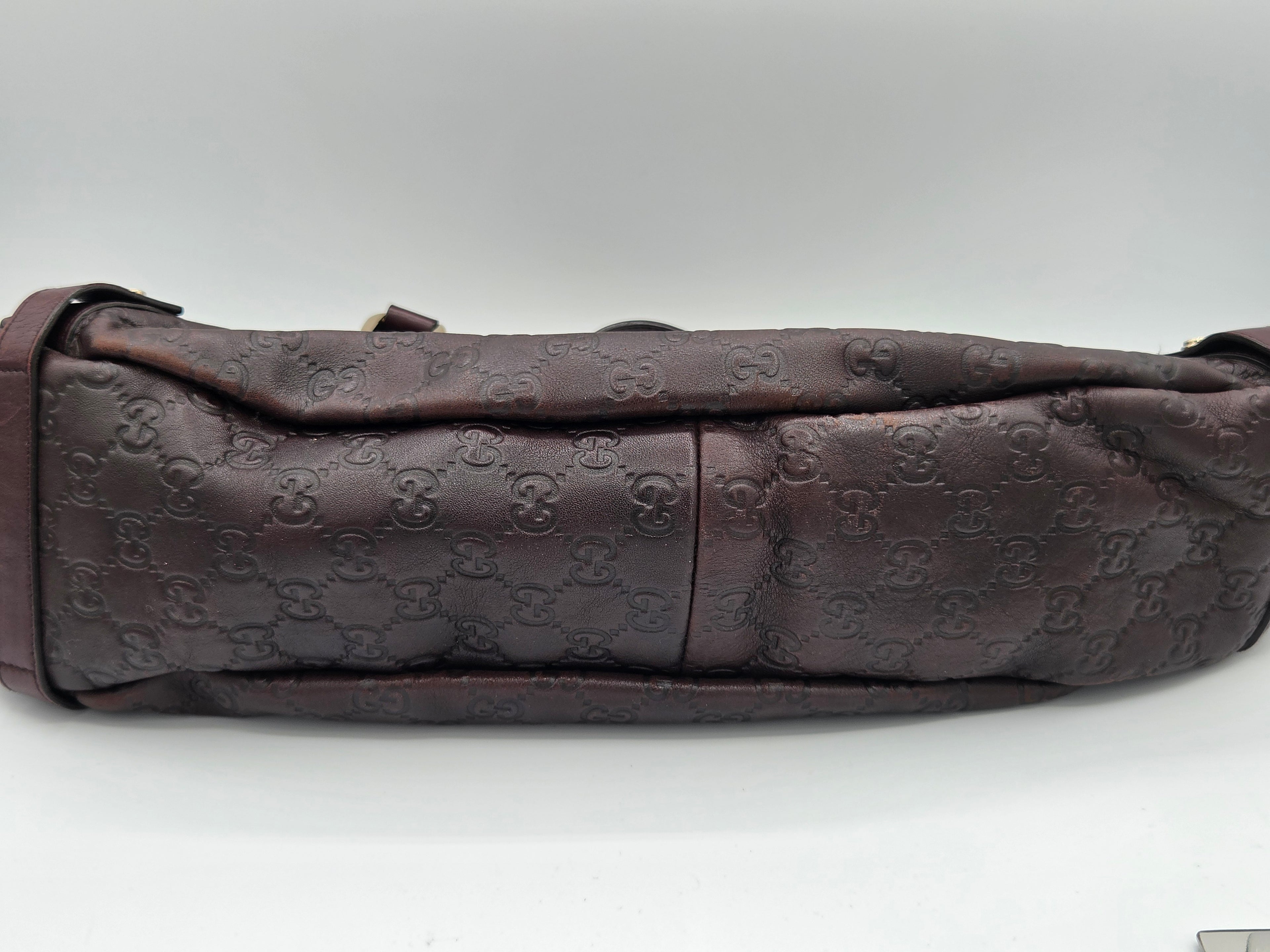 A dark brown Gucci shoulder bag featuring the brand's signature embossed GG monogram pattern, shown against a plain light gray background.