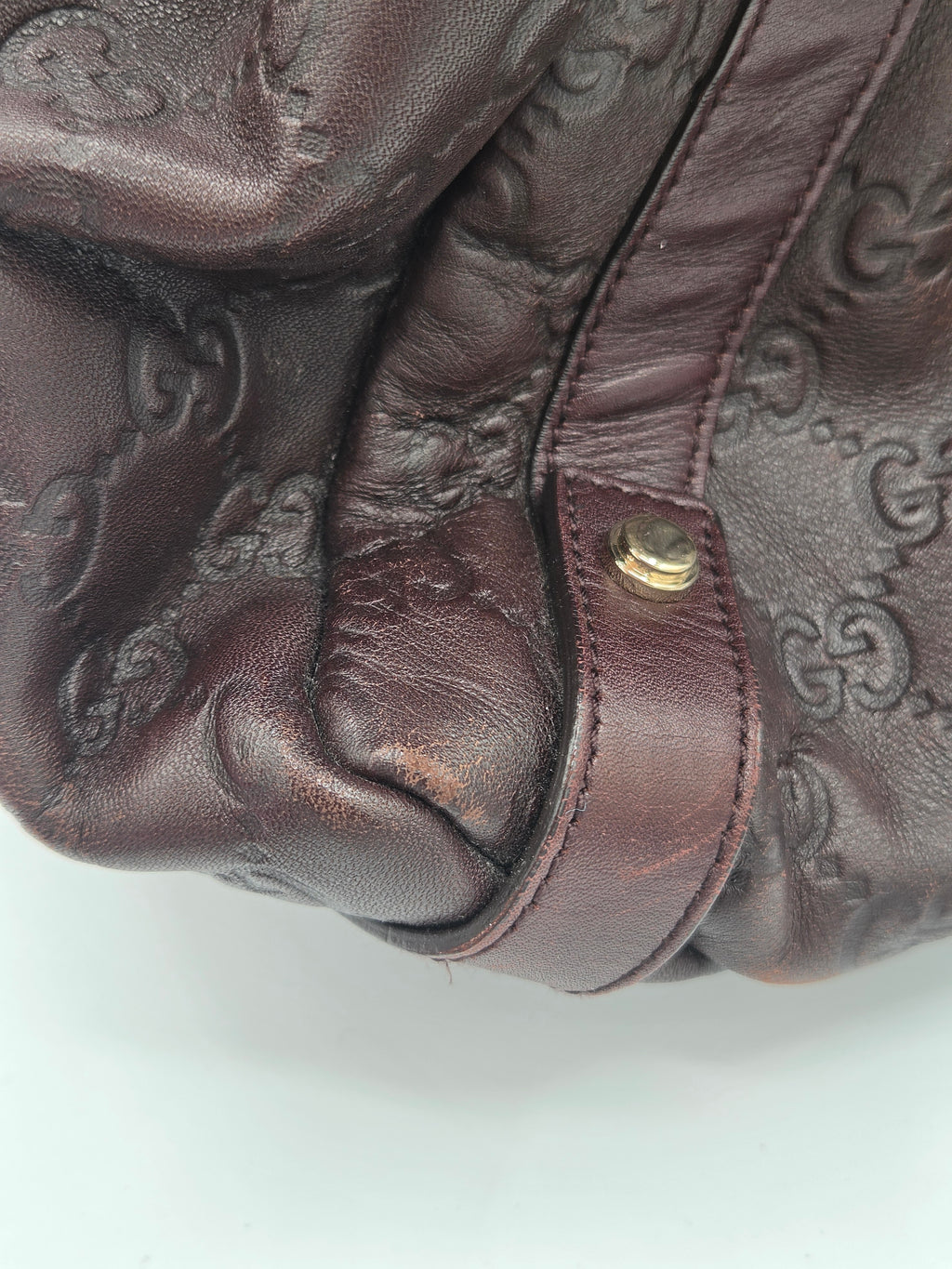 Close-up of a dark brown leather handbag featuring an embossed monogram pattern and a matching leather strap with a gold-tone snap button.