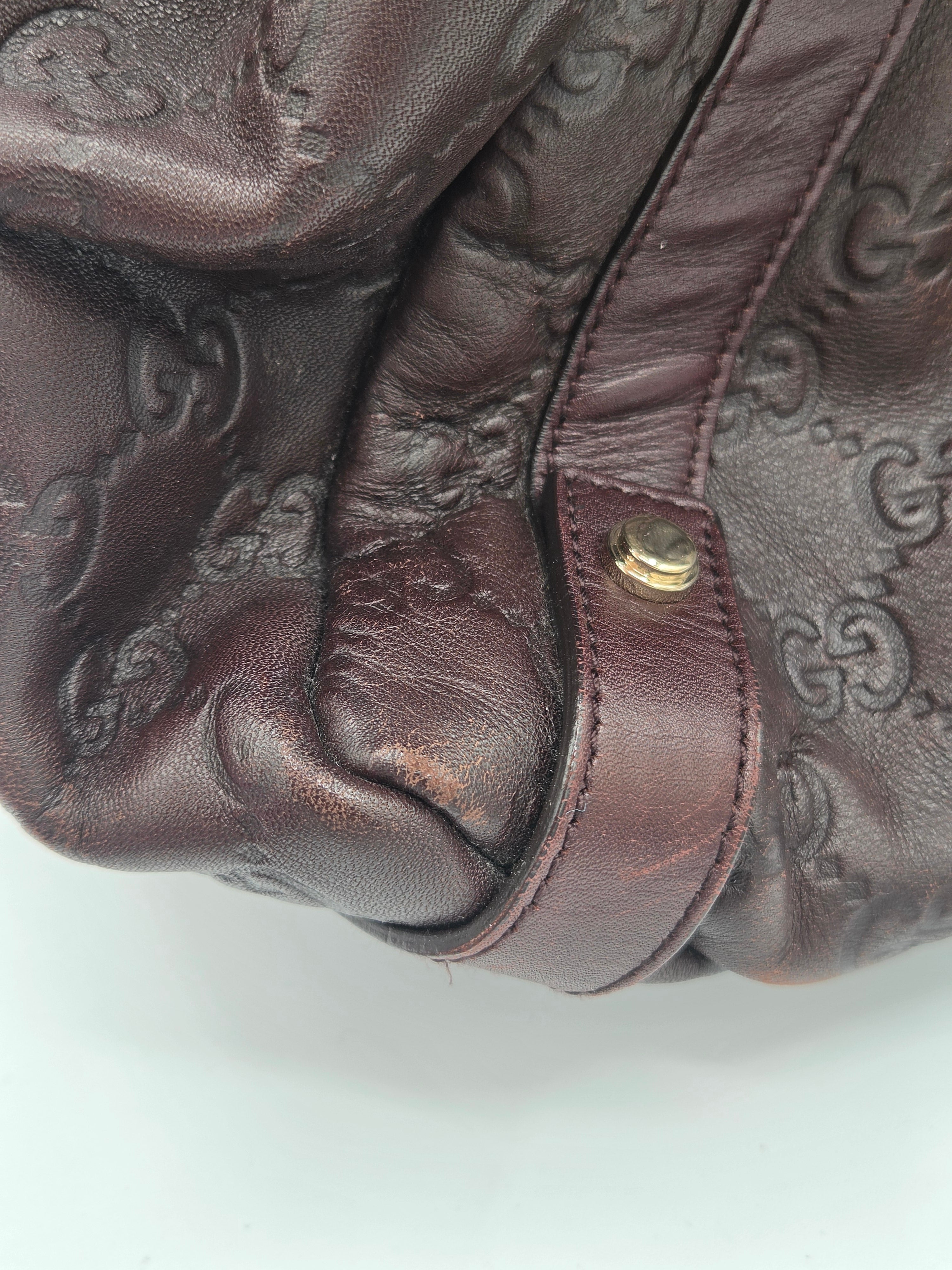 Close-up of a dark brown leather handbag featuring an embossed monogram pattern and a matching leather strap with a gold-tone snap button.