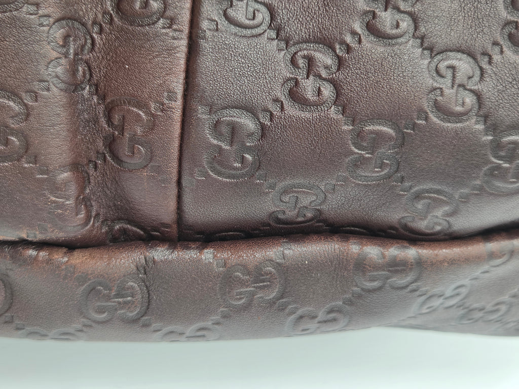 Close-up of a dark brown leather item featuring the embossed Gucci GG monogram pattern.