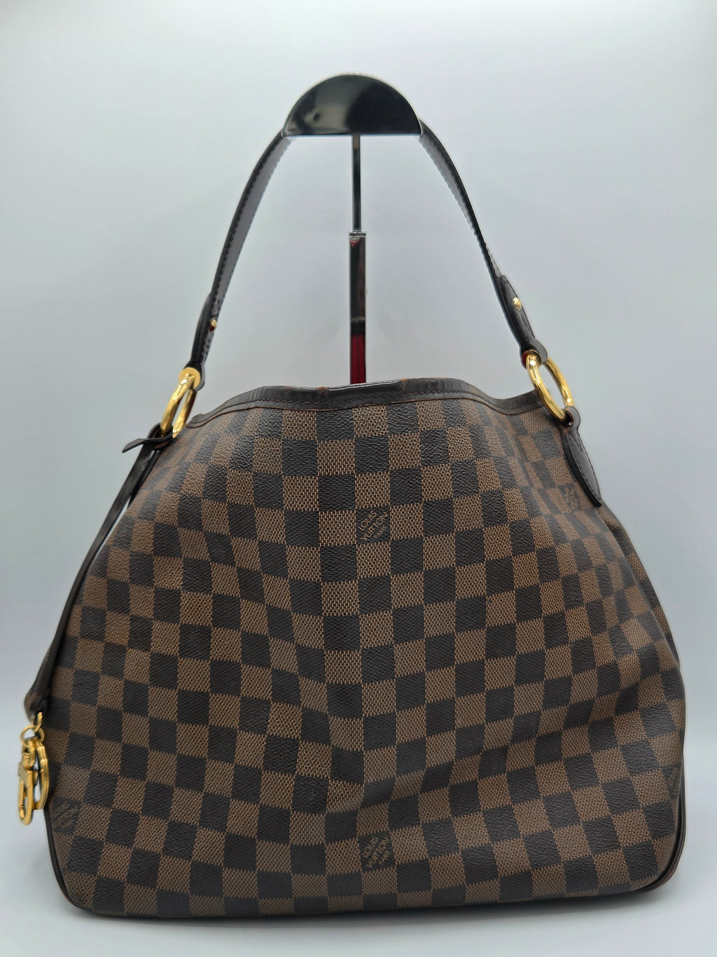 A brown and dark brown checkerboard handbag with gold-tone hardware and a black shoulder strap, photographed against a light gray background.