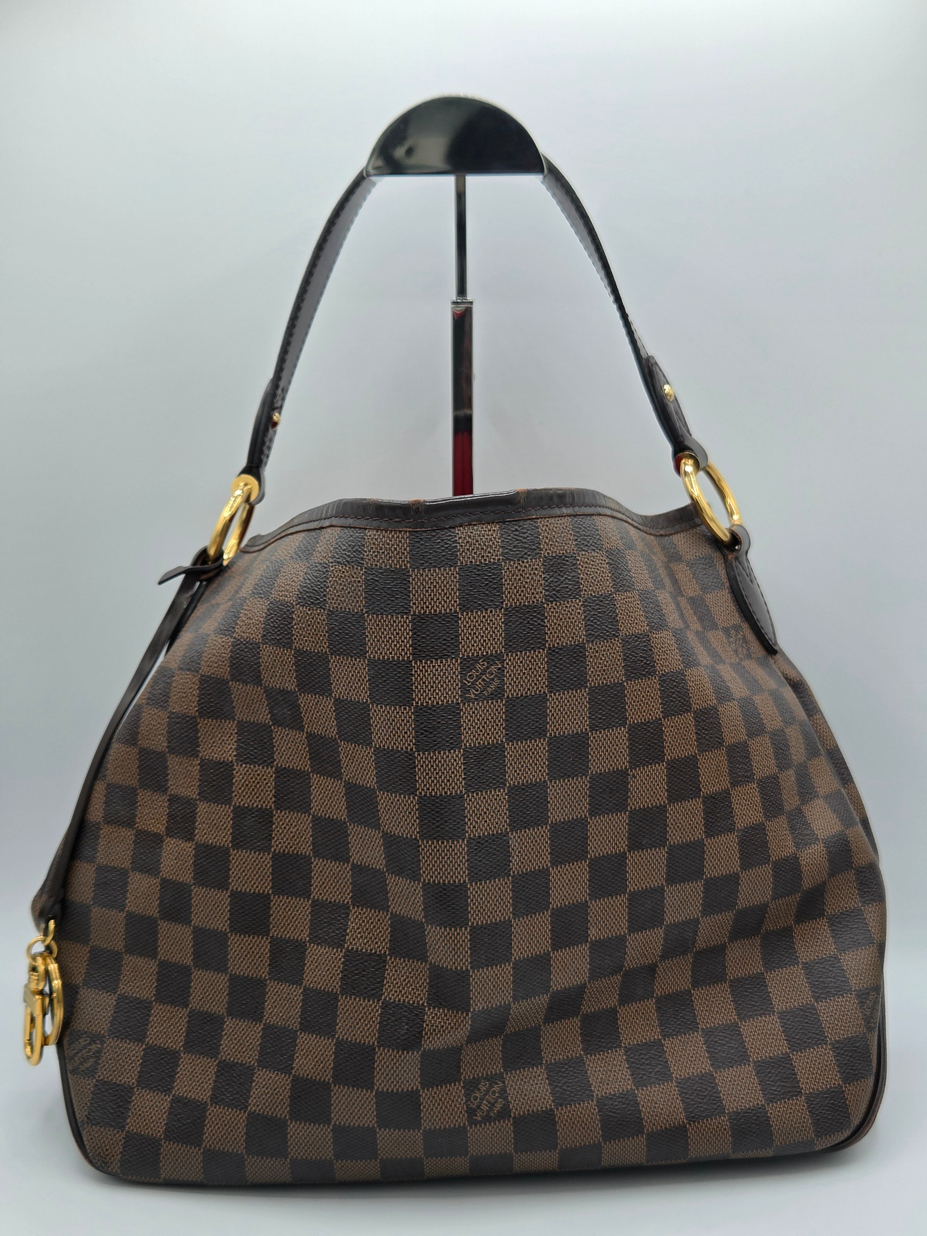 A brown and dark brown checkerboard handbag with gold-tone hardware and a black shoulder strap, photographed against a light gray background.