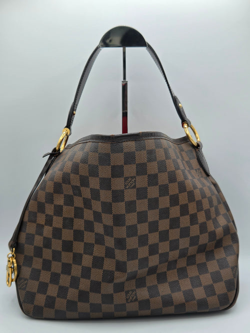 A brown and dark brown checkerboard handbag with gold-tone hardware and a black shoulder strap, photographed against a light gray background.