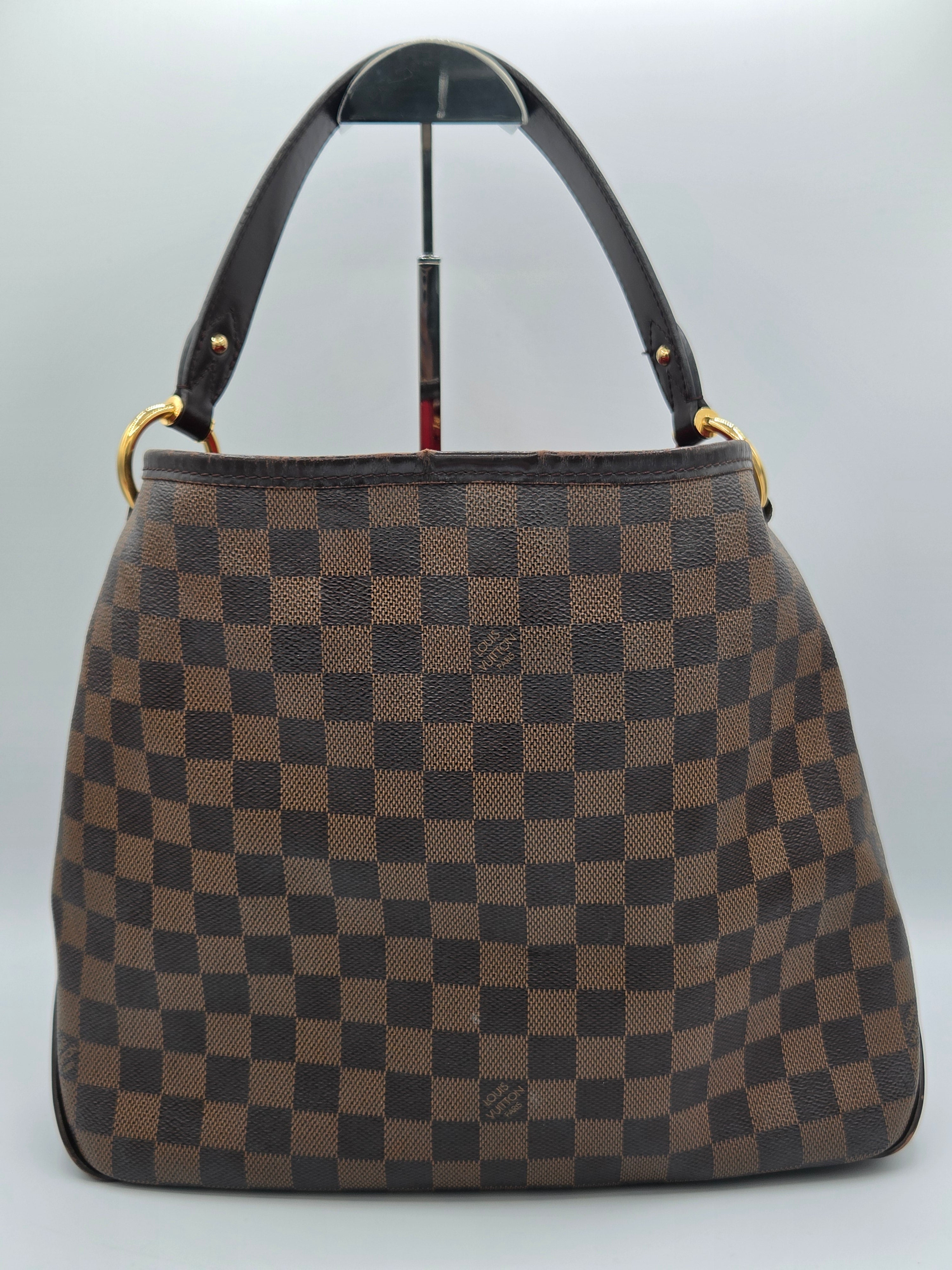 A brown and beige checkered handbag with a dark brown leather handle and gold-tone hardware, displayed on a light gray background.