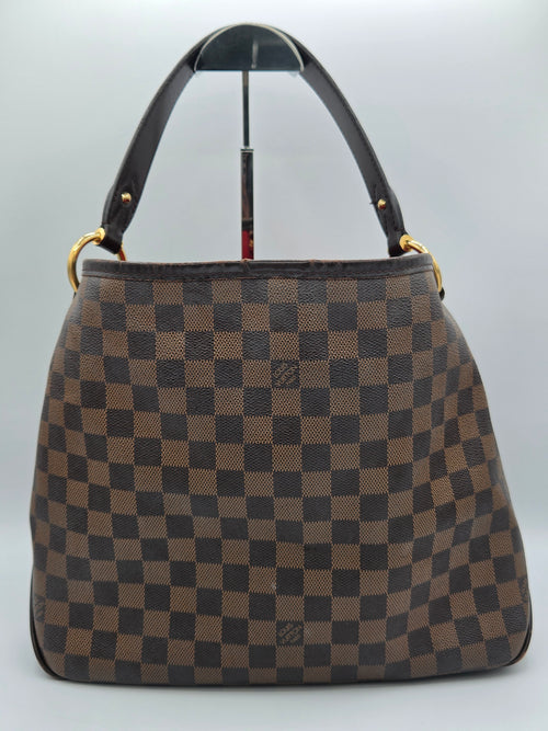 A brown and beige checkered handbag with a dark brown leather handle and gold-tone hardware, displayed on a light gray background.