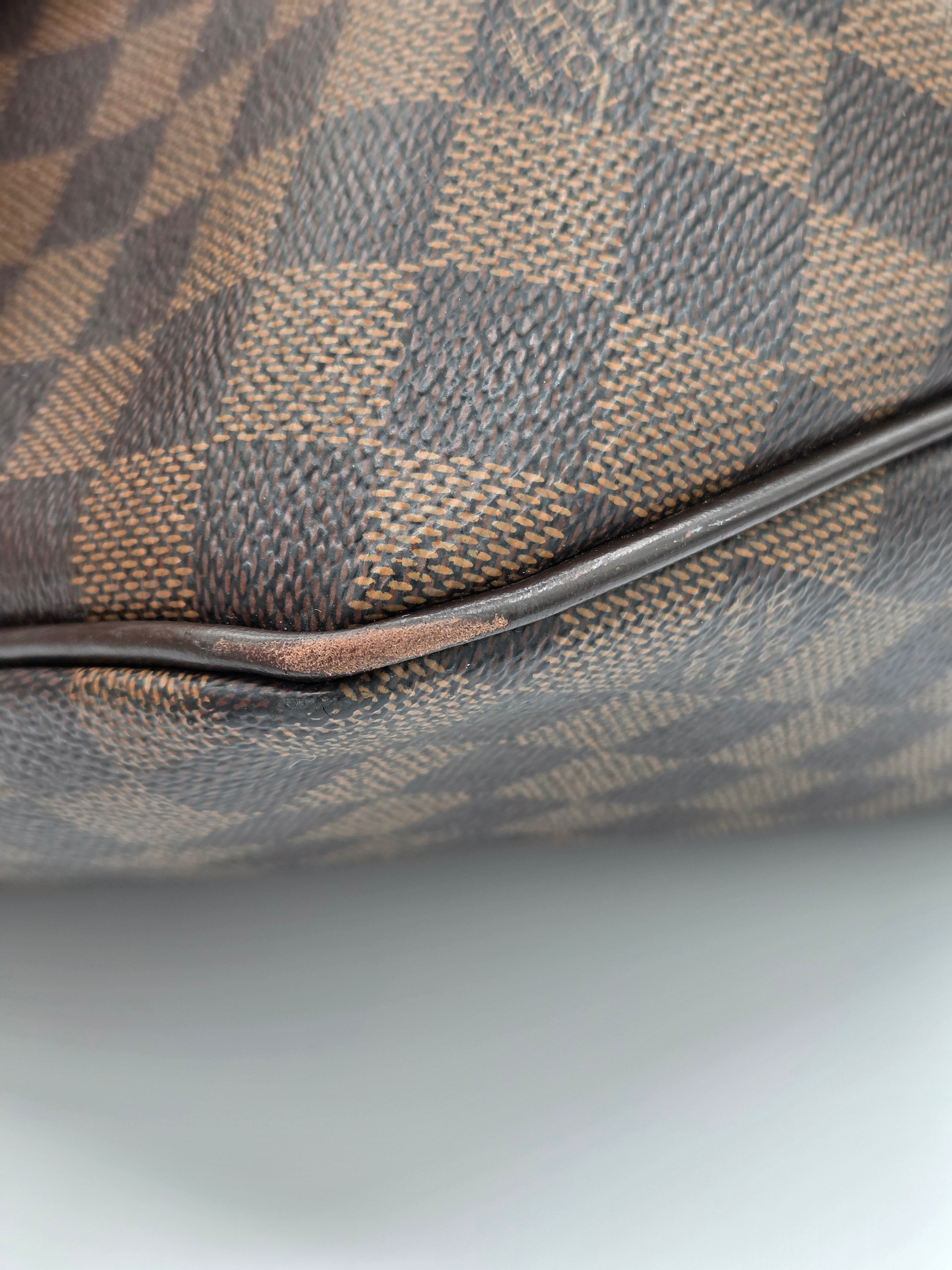 Close-up of a Louis Vuitton Damier canvas bag corner showing the classic brown and beige checkerboard pattern and a dark brown leather piping edge.