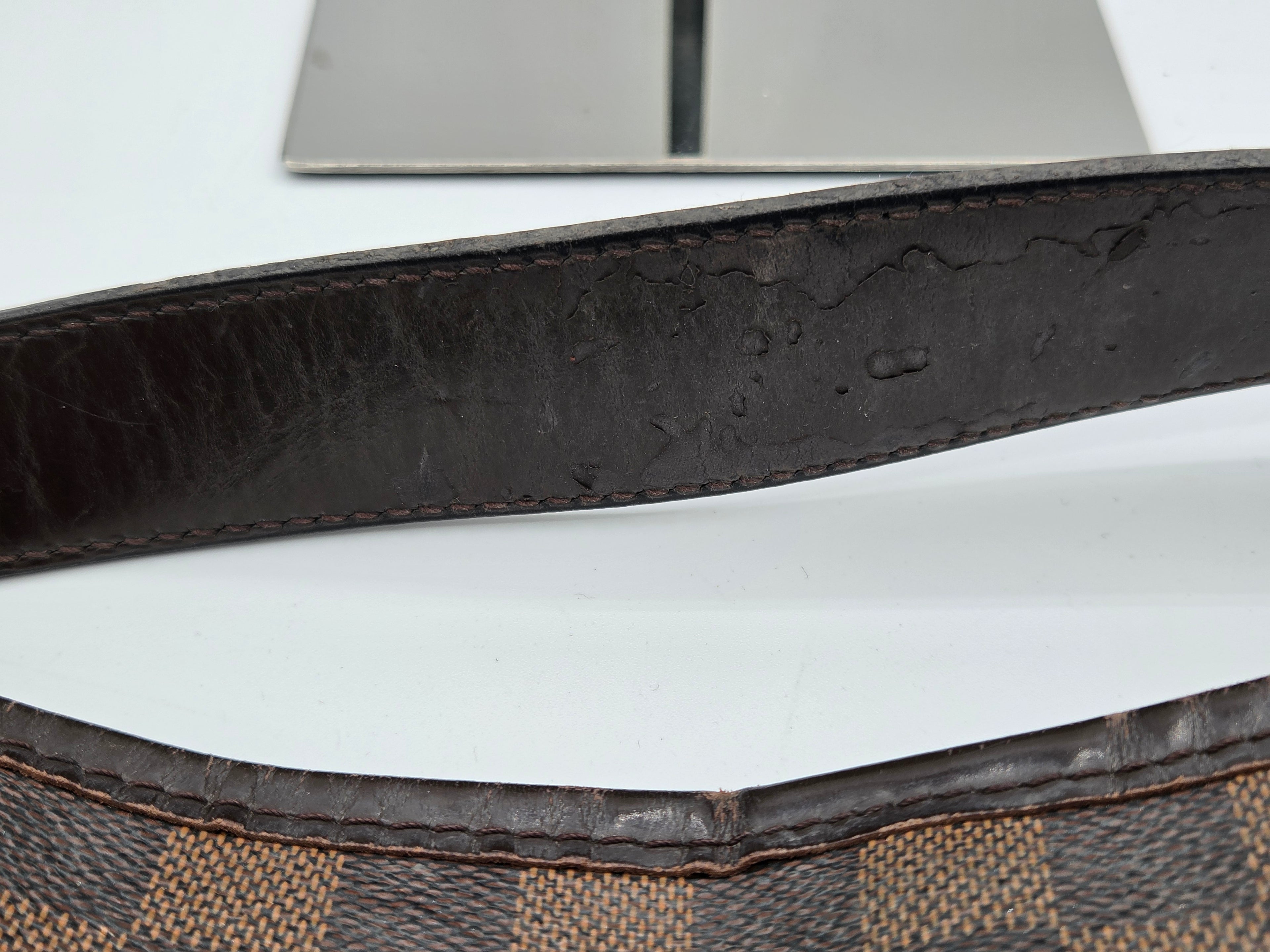 Close-up of a dark brown leather strap with visible wear and scuffs, laid over a brown and beige checkered fabric surface.
