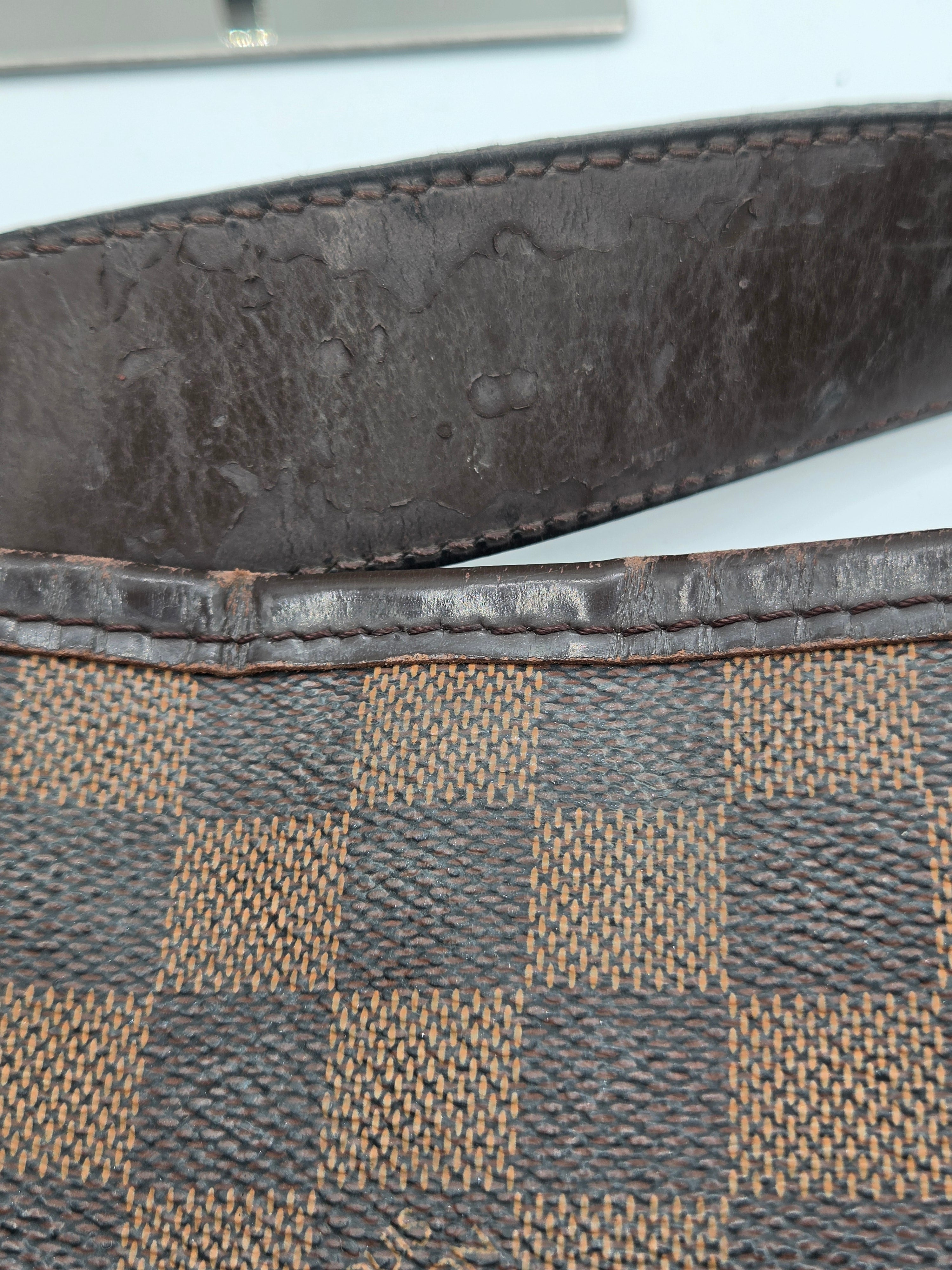 Close-up of a dark brown leather strap next to a dark brown and beige checkered canvas material, likely part of a designer bag.