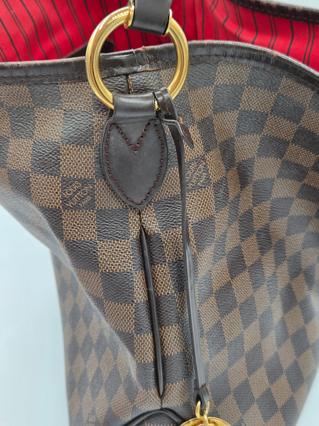 Close-up of a Louis Vuitton handbag in Damier Ebene canvas, showing the brown and beige checkered pattern, dark brown leather trim, and gold-tone hardware.