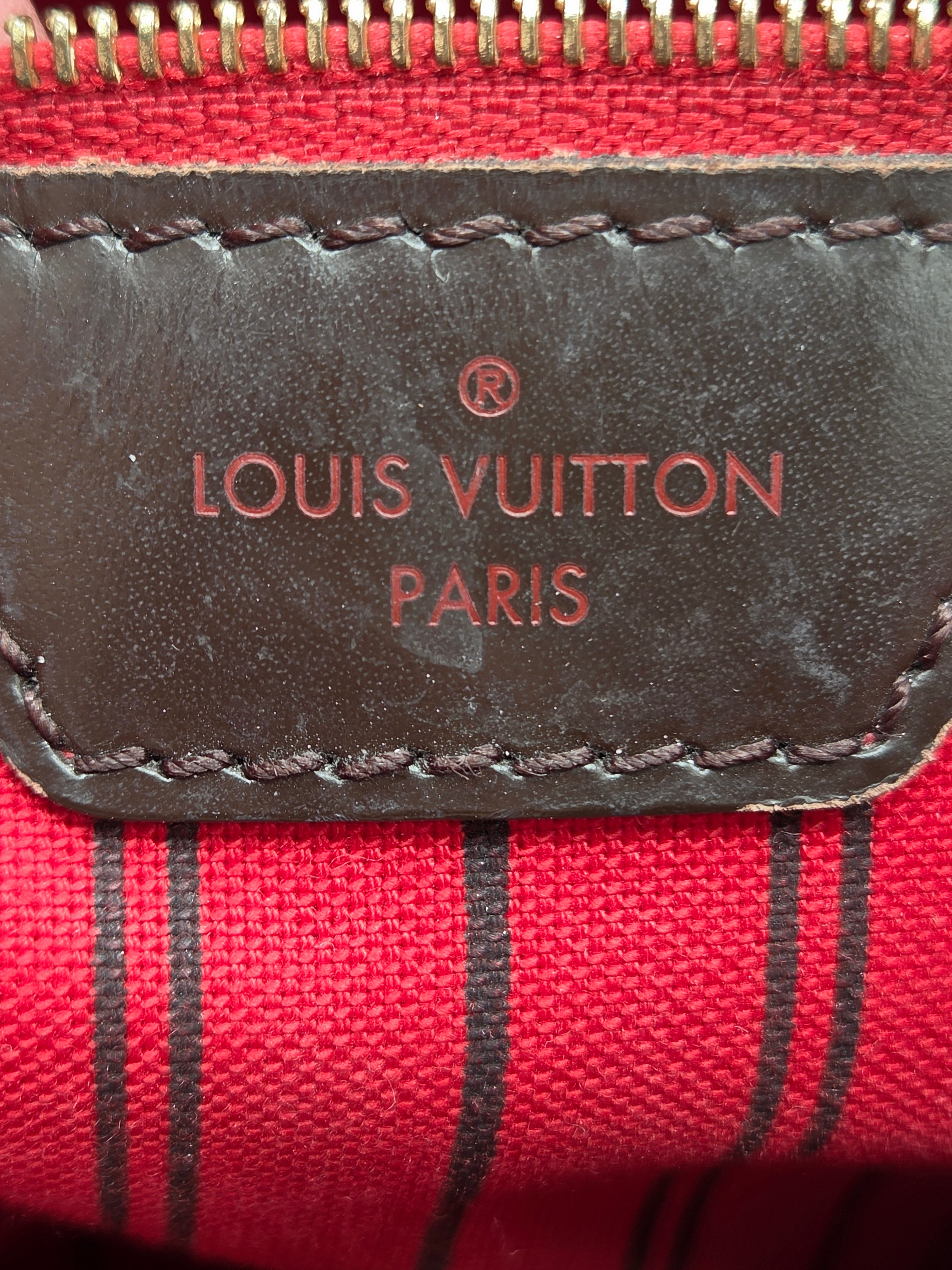 Close-up of a Louis Vuitton pouch showing a dark brown leather patch with embossed red 'LOUIS VUITTON PARIS' text, stitched onto a red canvas background with thin black vertical stripes.