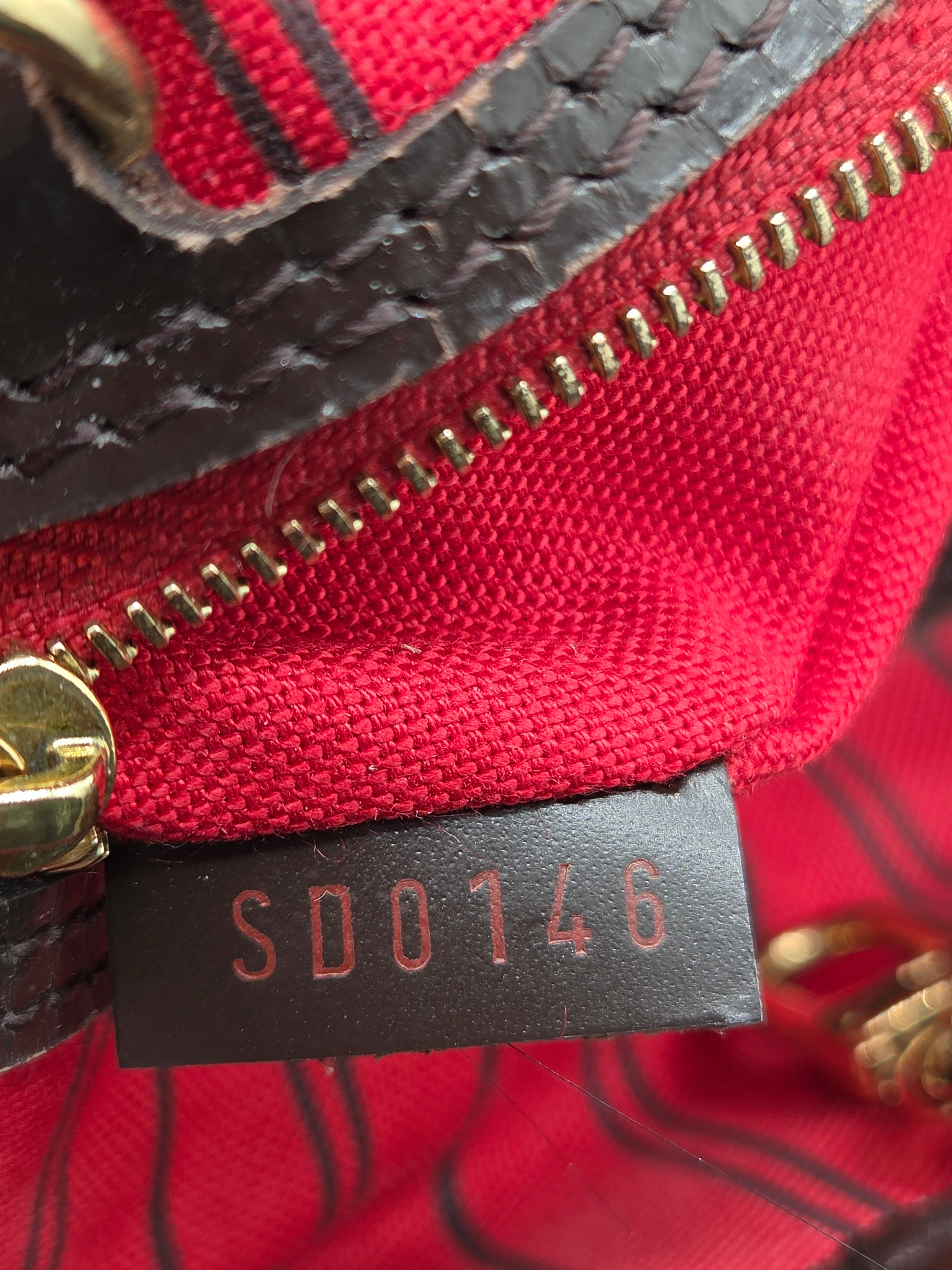 Close-up of a red woven fabric bag with a black leather tag stamped with the number 146DD0146, a gold zipper, and a gold metal pull.