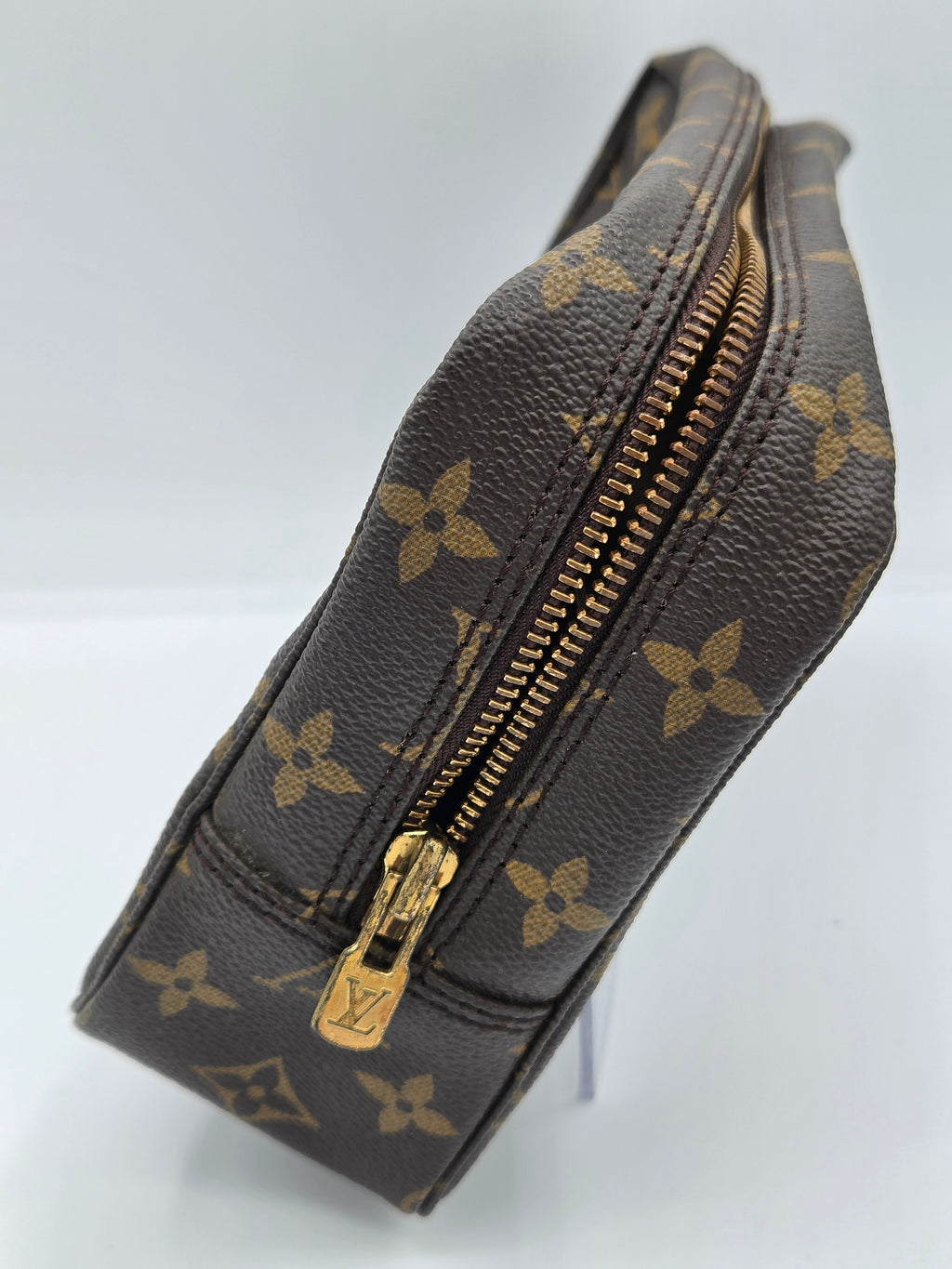 A Louis Vuitton monogram canvas pouch with a gold-tone zipper, shown on a light gray background.