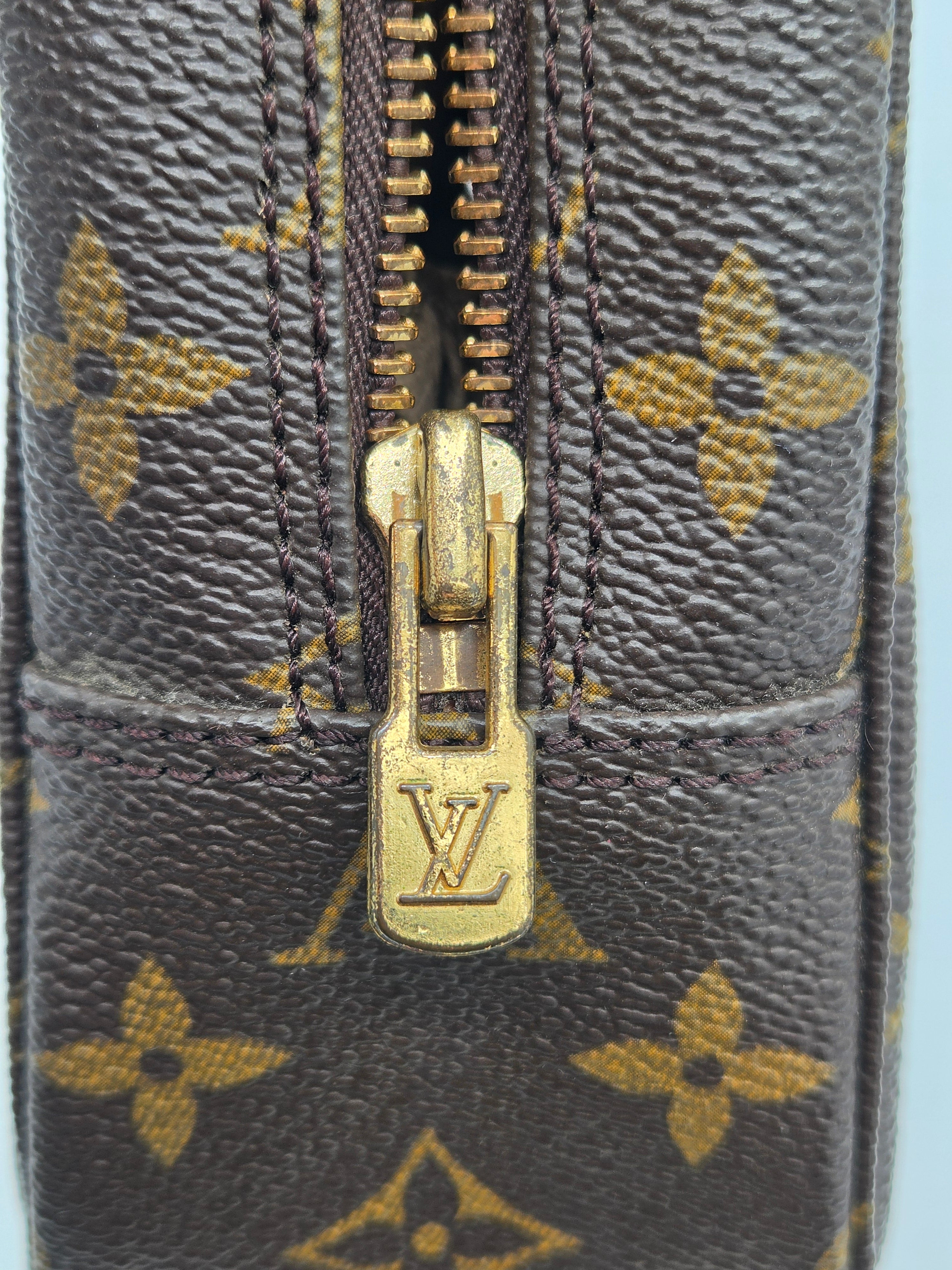 Close-up of a Louis Vuitton monogram canvas zipper with a gold-tone metal pull tab featuring the embossed LV logo.