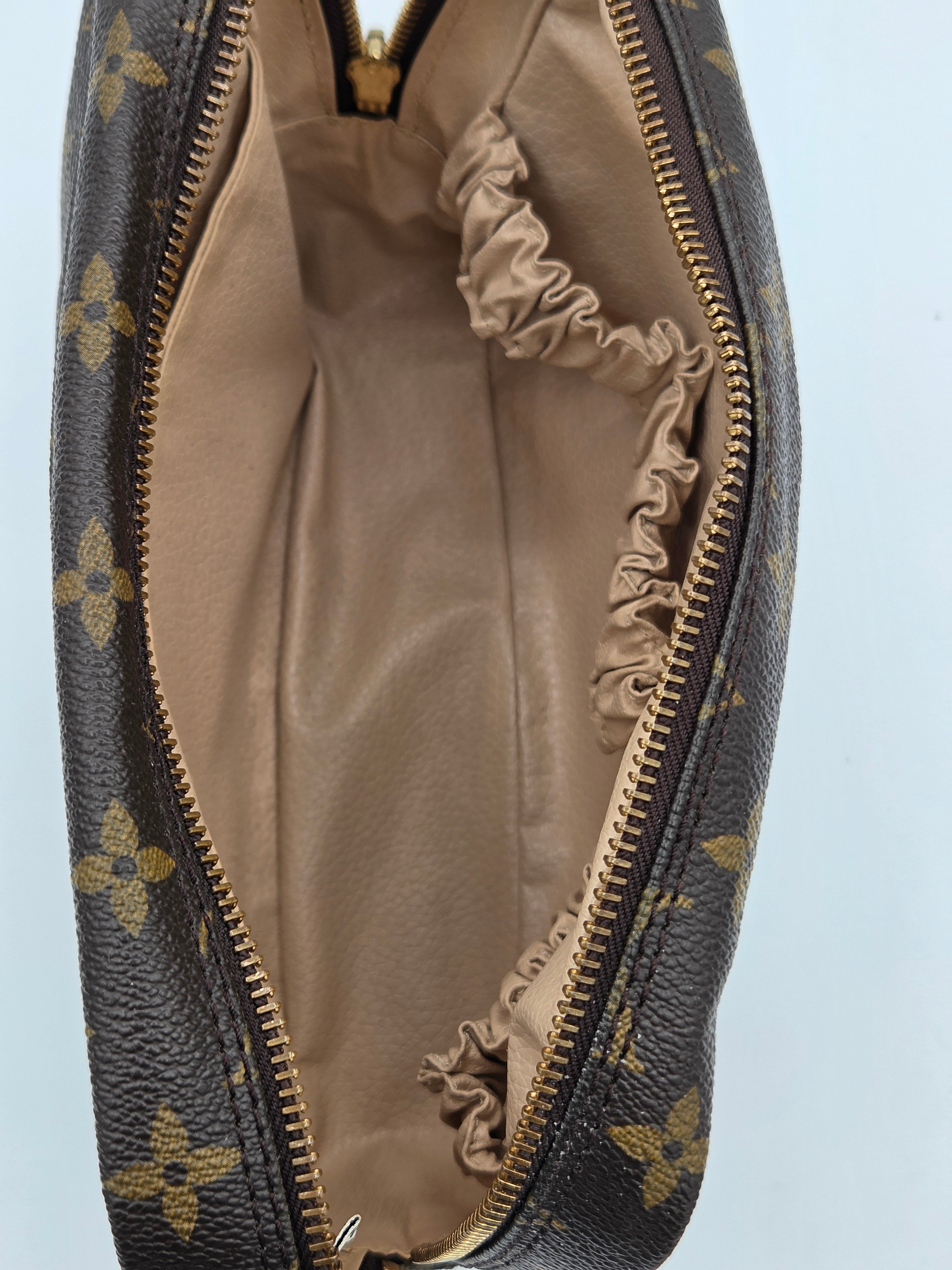 Close-up of an open Louis Vuitton monogram pouch showing the beige interior lining and gold-tone zipper.