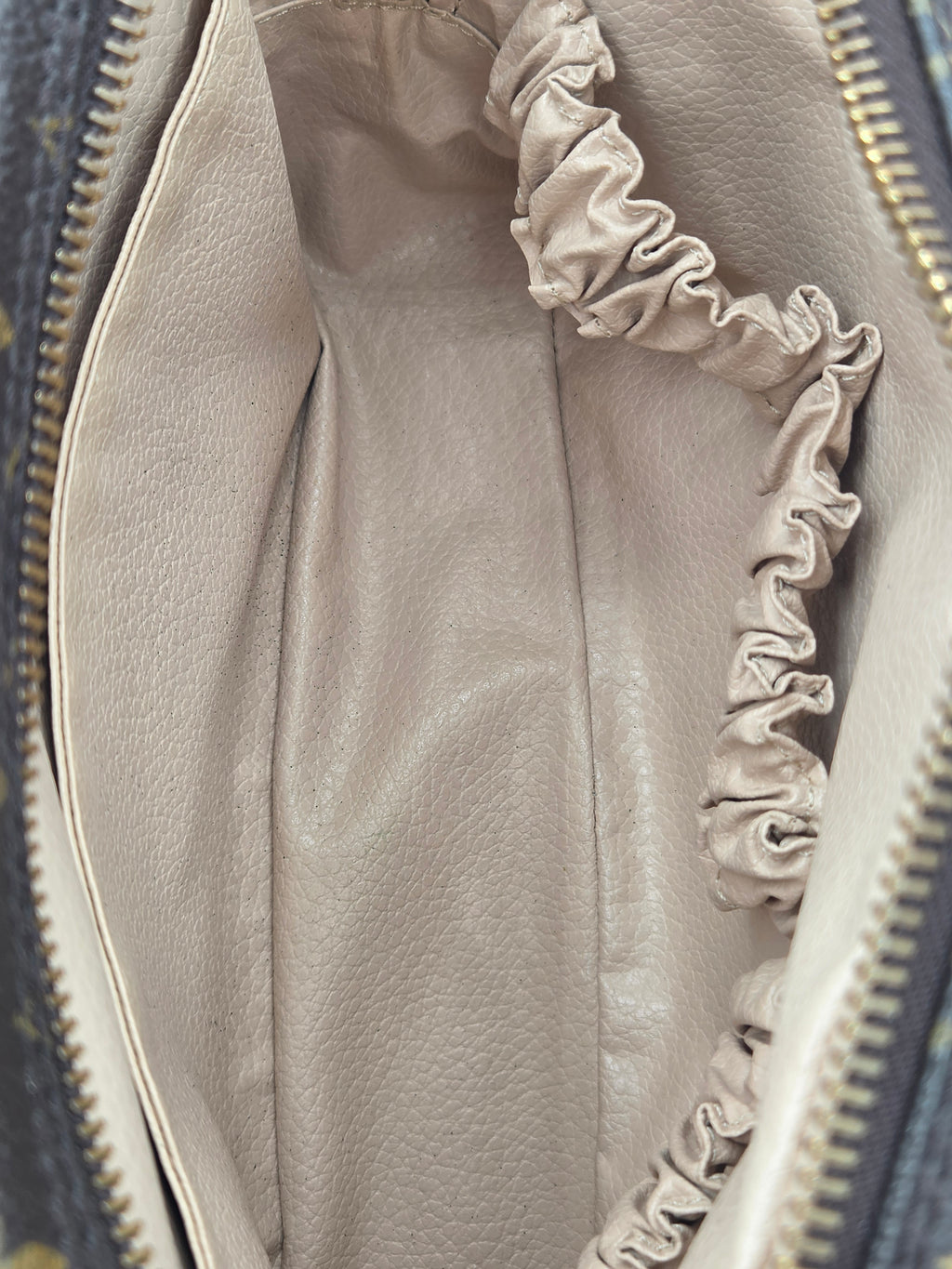 Close-up of the interior of a handbag showing a light beige pebbled leather lining with a gathered elastic pocket and gold-tone zipper.