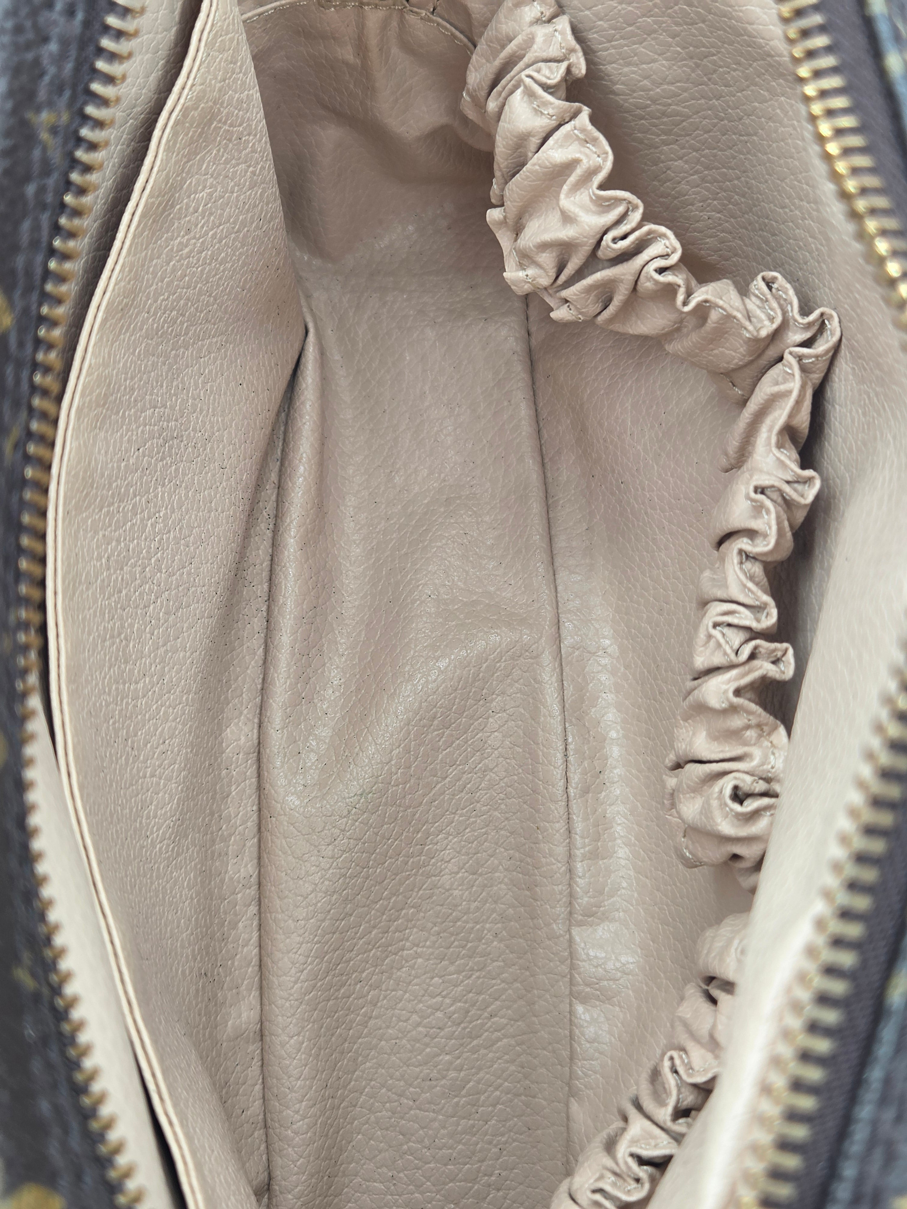 Close-up of the interior of a handbag showing a light beige pebbled leather lining with a gathered elastic pocket and gold-tone zipper.