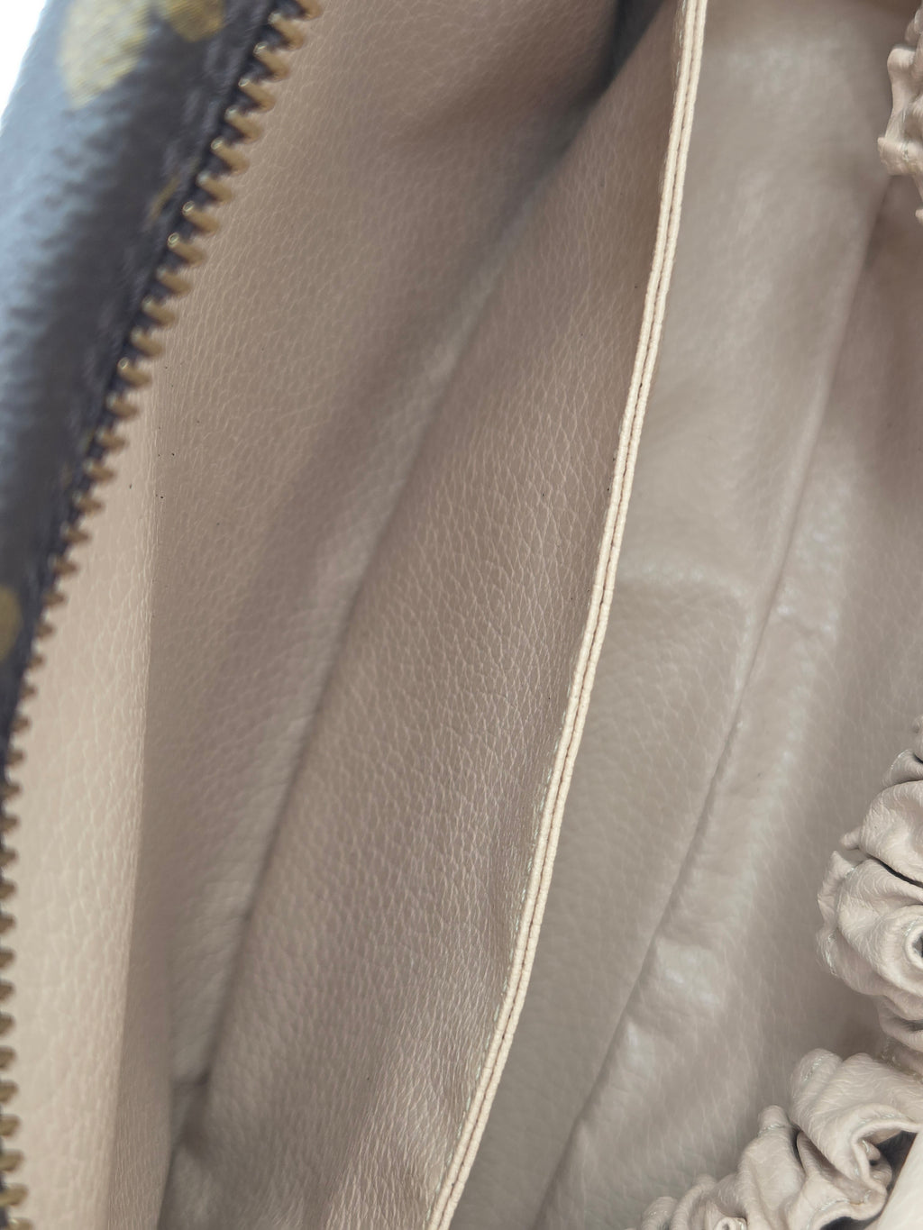Close-up of a beige leather interior pouch with a gold zipper and decorative ruffled trim.