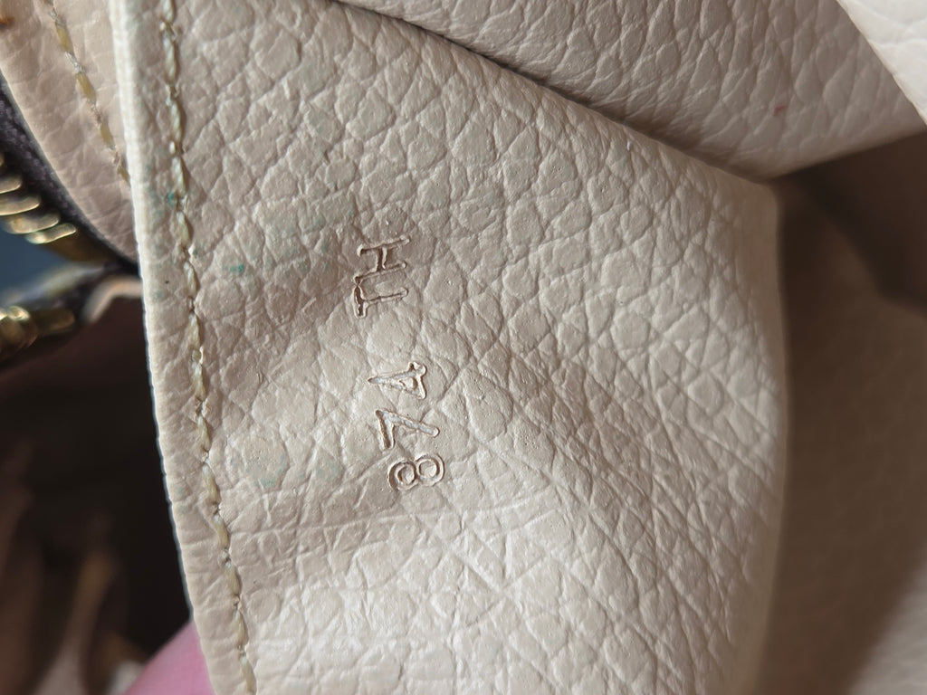 Close-up of a light beige pebbled leather interior corner with stitched edges and embossed serial numbers 'H1748'.