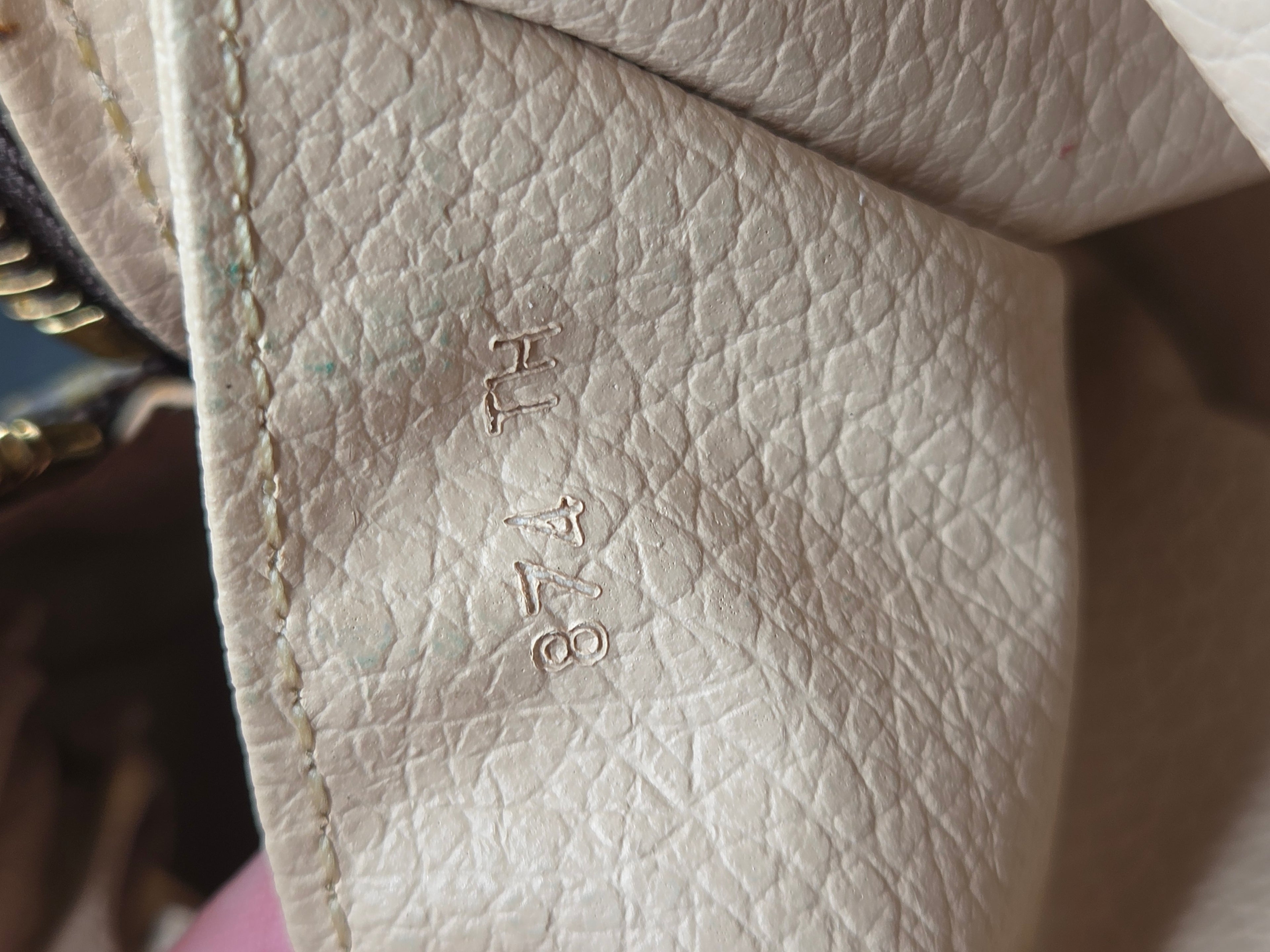 Close-up of a light beige pebbled leather interior corner with stitched edges and embossed serial numbers 'H1748'.