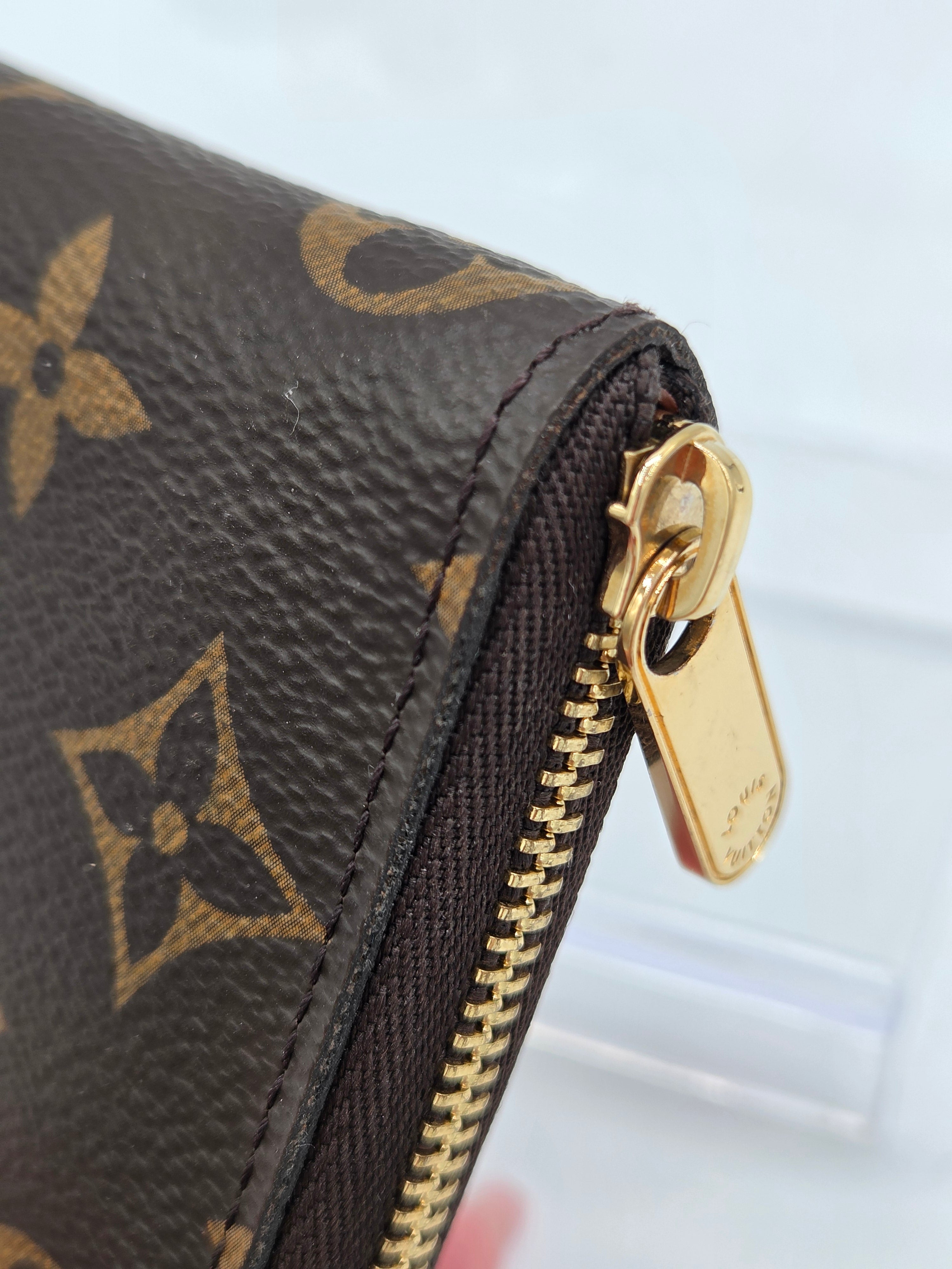 Close-up of a Louis Vuitton monogram wallet corner with a gold-tone zipper pull and dark brown coated canvas.