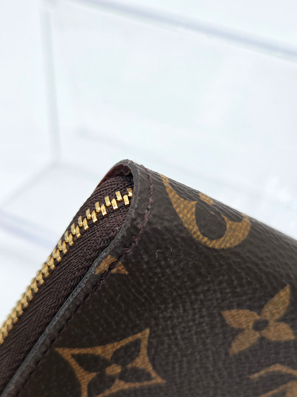 Close-up of a Louis Vuitton monogram canvas zippered pouch showing the dark brown coated canvas, tan printed monogram pattern, and gold-tone zipper.