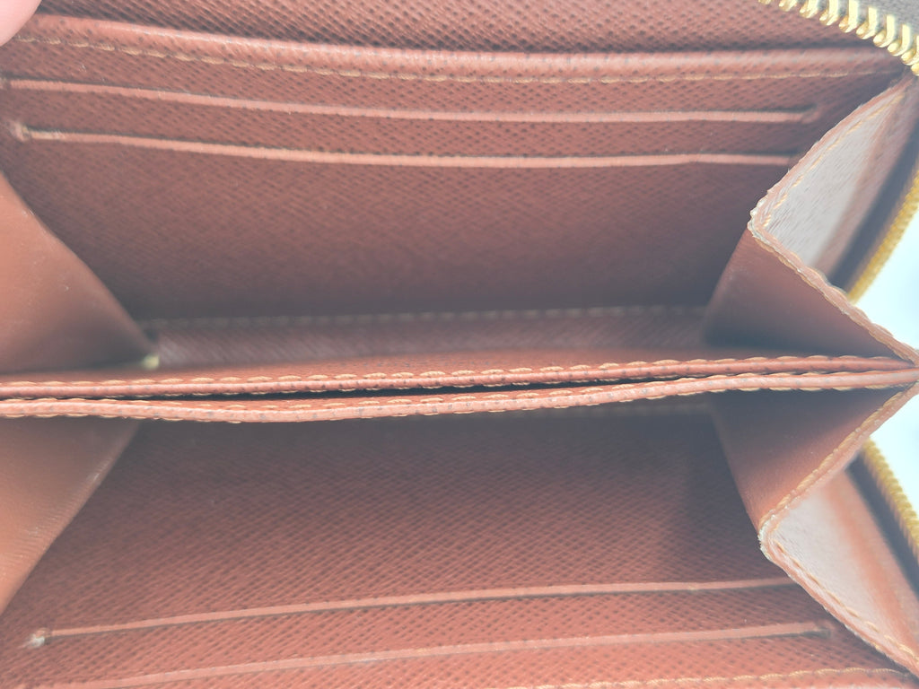 Close-up of the interior of a brown leather wallet showing card slots, a divider, and a gold zipper.