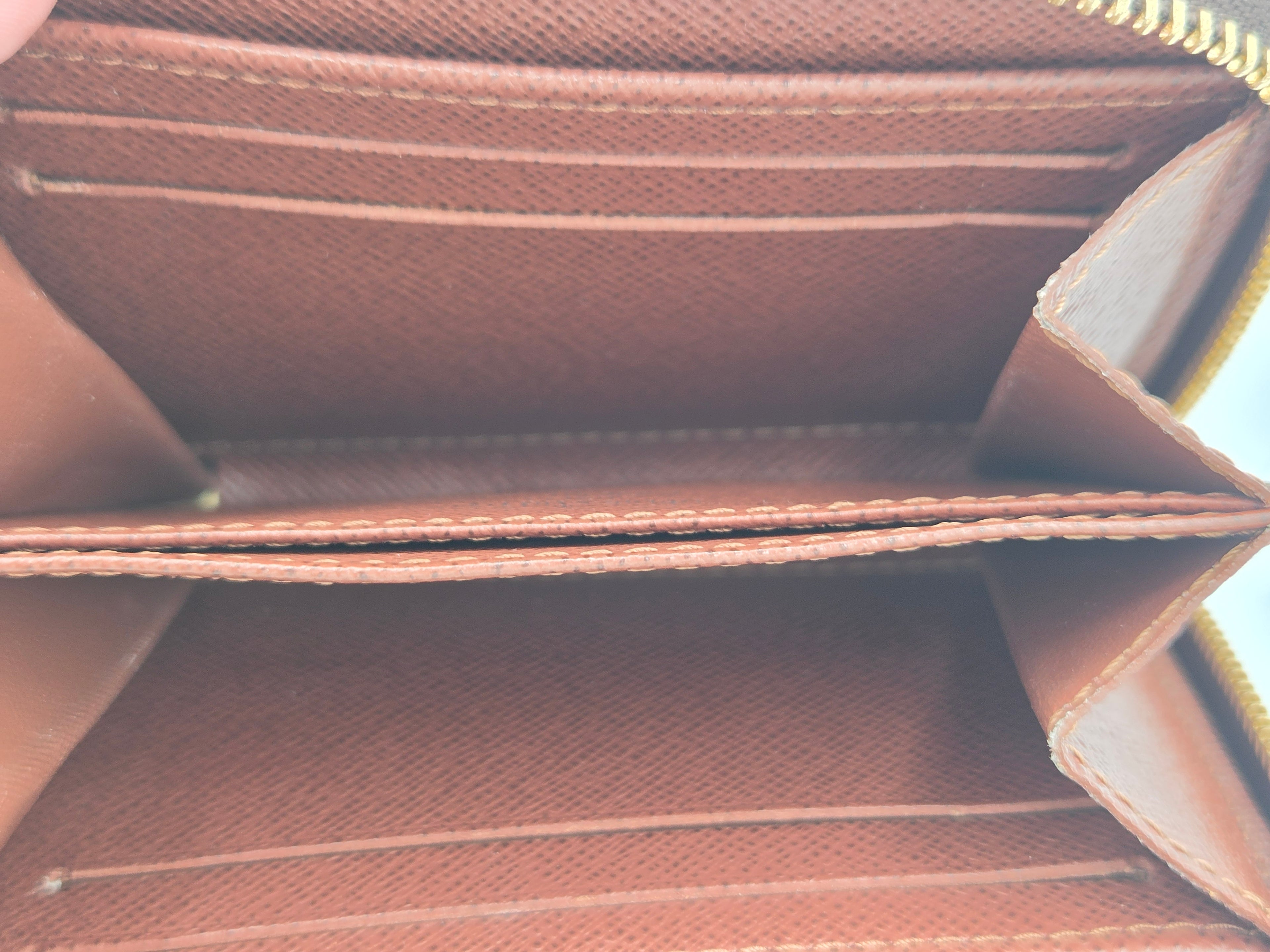 Close-up of the interior of a brown leather wallet showing card slots, a divider, and a gold zipper.