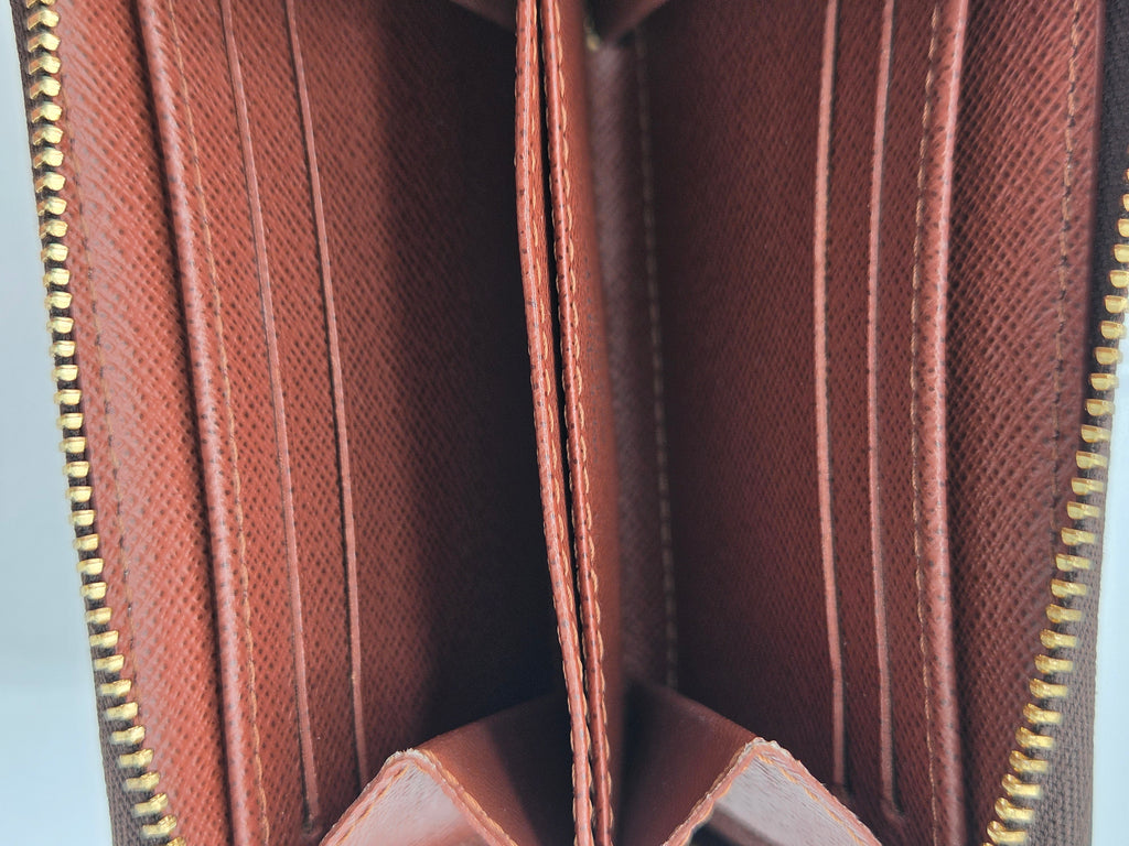 Close-up of the interior of a brown textured leather wallet, showing multiple card slots, vertical divider panels, and gold-tone zipper edges.
