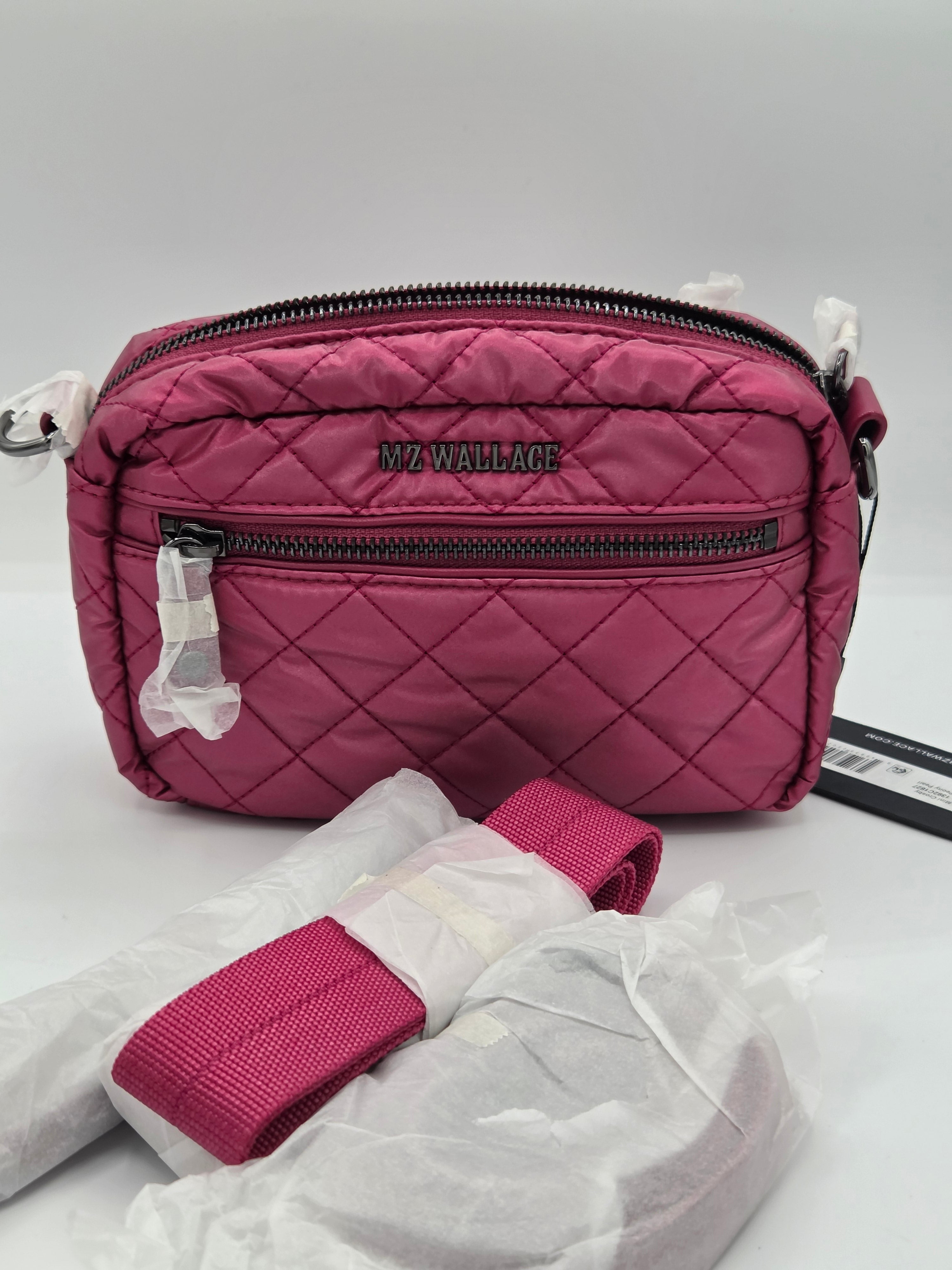 A pink quilted nylon crossbody bag by MZ Wallace, featuring a diamond-quilted pattern, black zippers, and a matching pink webbed strap resting in front on white tissue paper.
