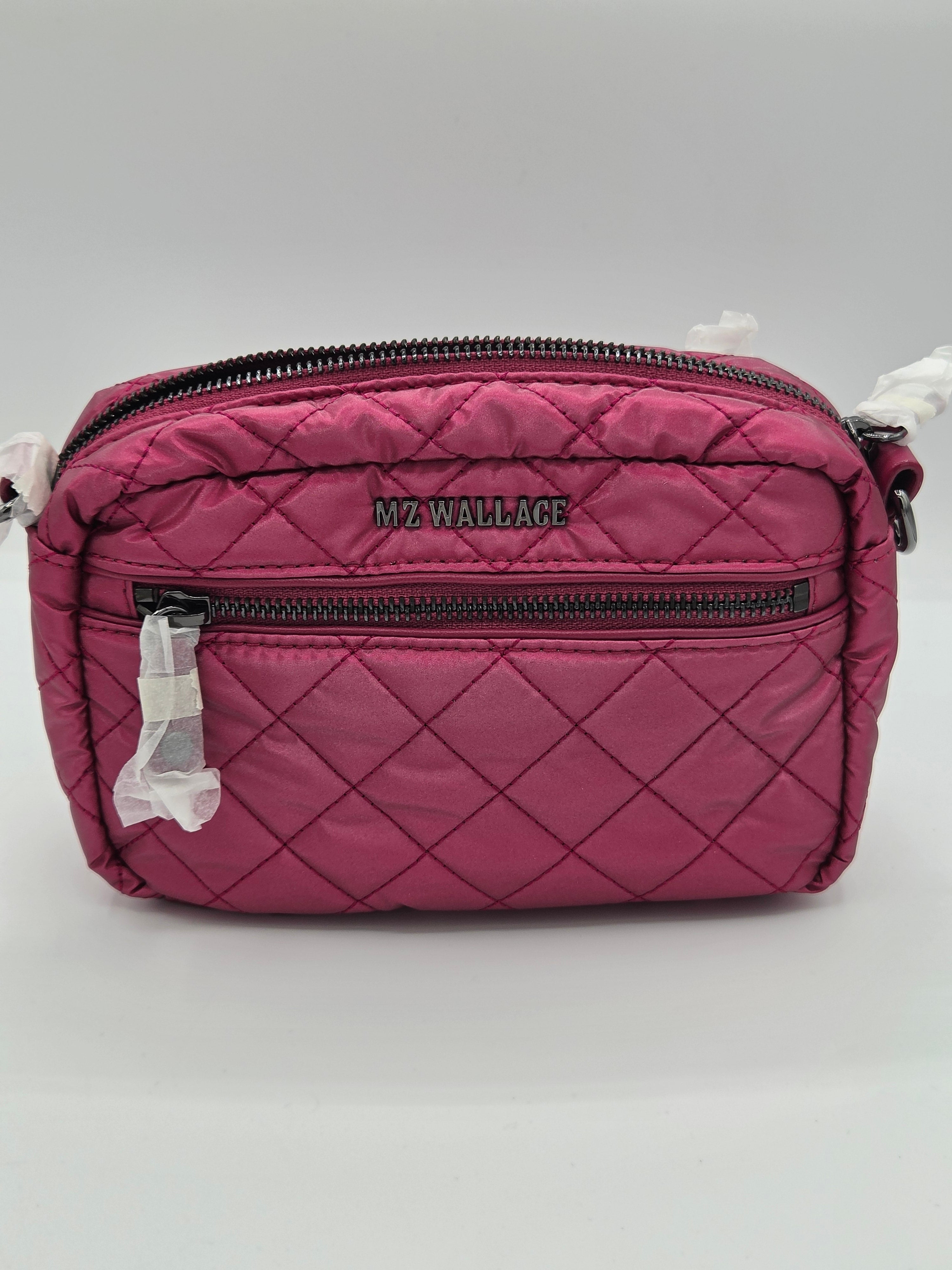 A pink quilted crossbody bag with black zippers and the brand name 'MZ WALLACE' printed on the front, shown on a light gray background with protective plastic still attached to the zipper pulls.
