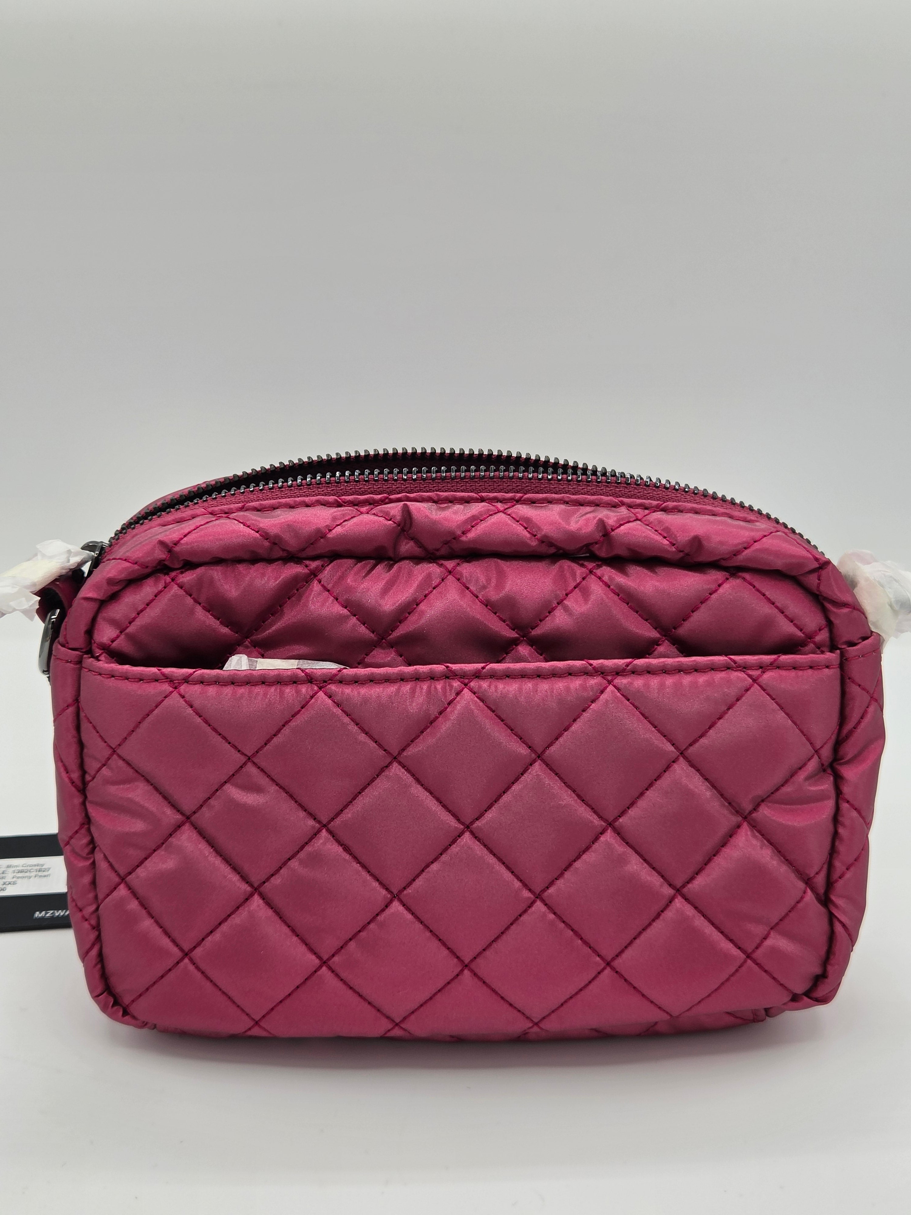 A quilted magenta pink nylon cosmetic pouch with a diagonal zipper, shown on a neutral gray background.