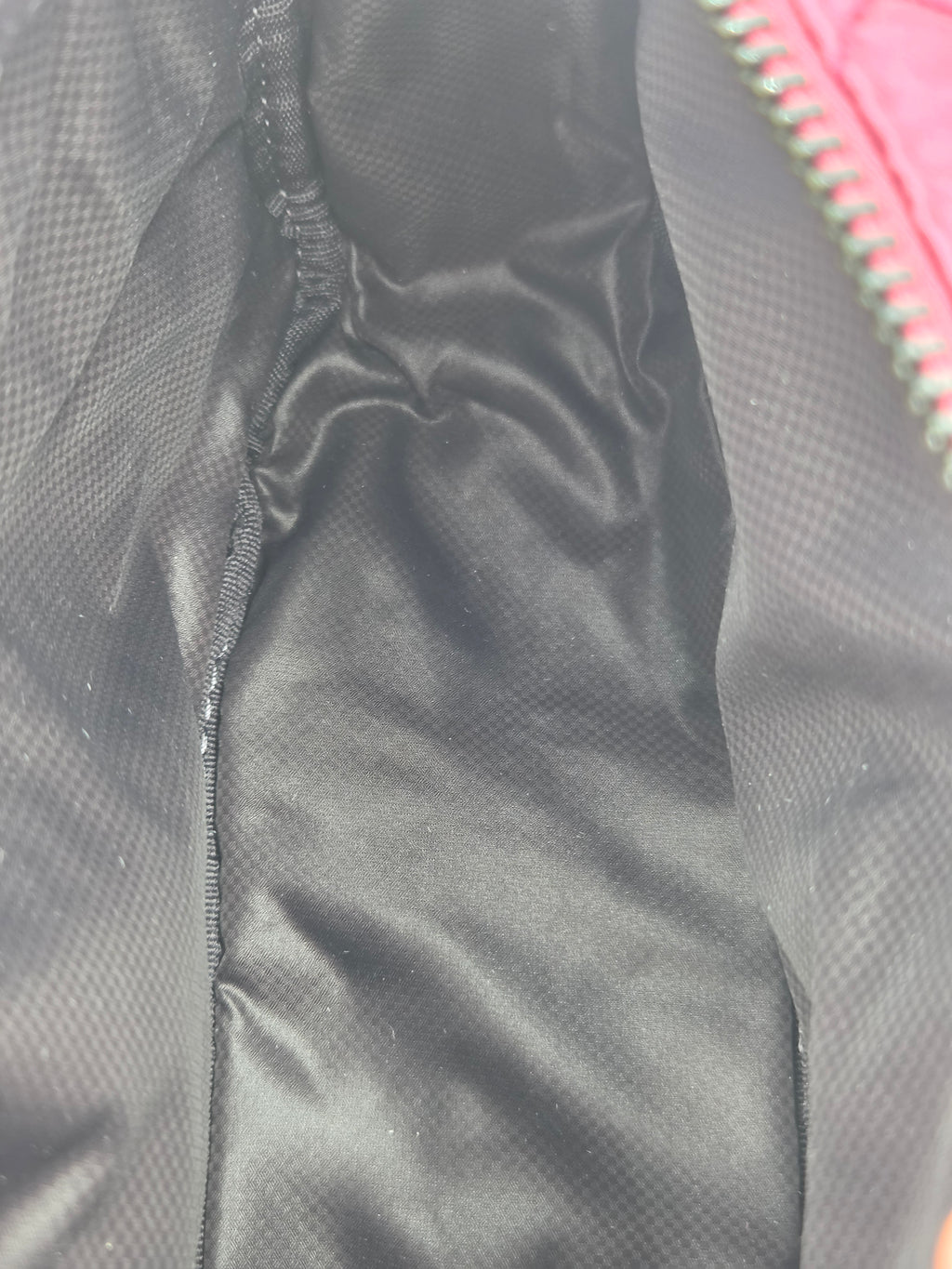 Close-up of the interior lining of a black quilted puffer jacket, showing the satin-like fabric and a glimpse of a pink exterior zipper.