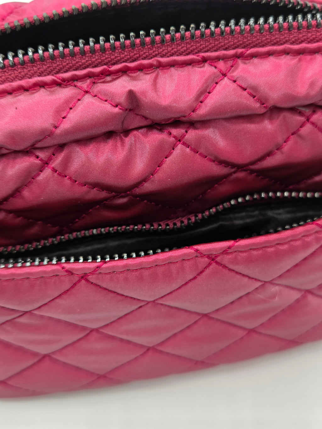 Close-up of a quilted pink nylon pouch with silver zippers and a black interior lining.