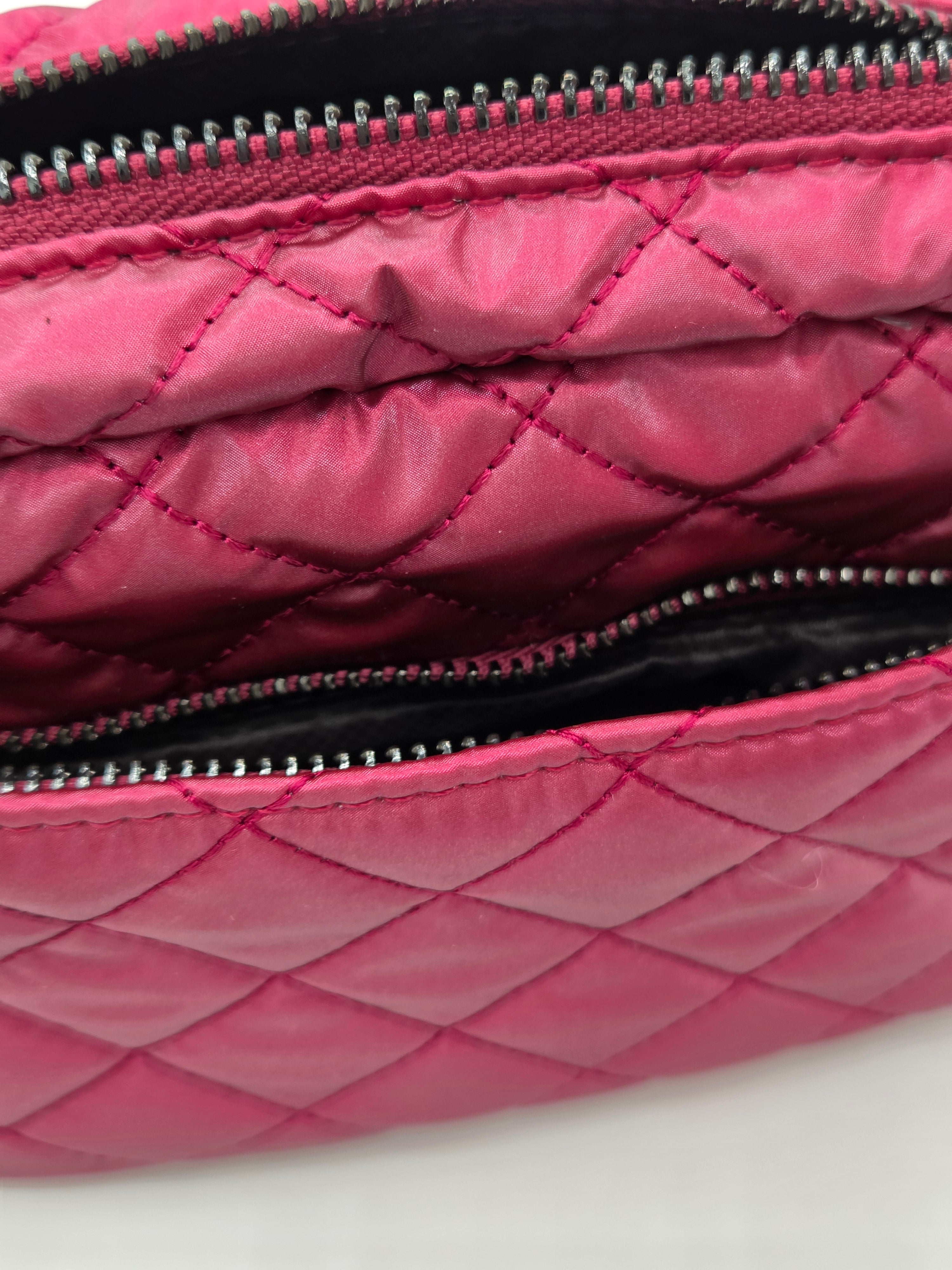 Close-up of a quilted pink nylon pouch with silver zippers and a black interior lining.