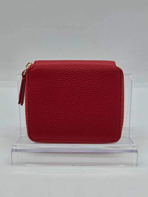 A red pebbled leather zip-around coin purse with a gold-tone zipper pull, displayed on a clear acrylic stand against a light gray background.