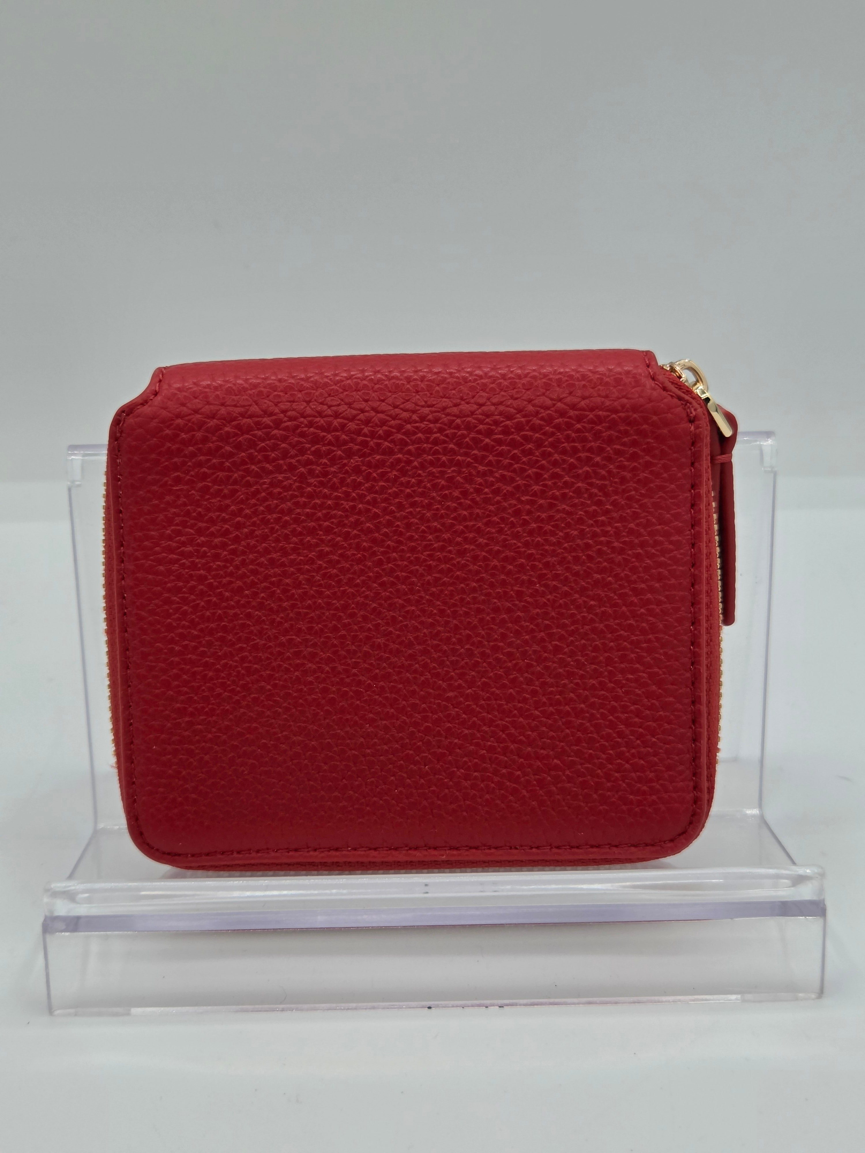 A red pebbled leather zip-around wallet with a gold-tone zipper pull, displayed on a clear acrylic stand against a neutral gray background.