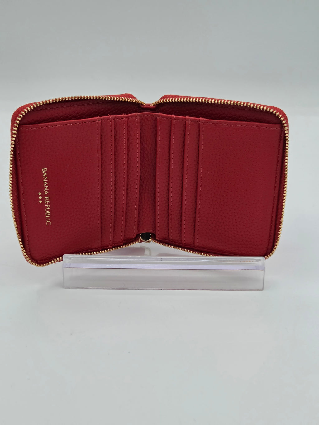 An open red leather zip-around wallet with multiple card slots and gold-tone zippers, displayed on a clear acrylic stand against a light gray background.