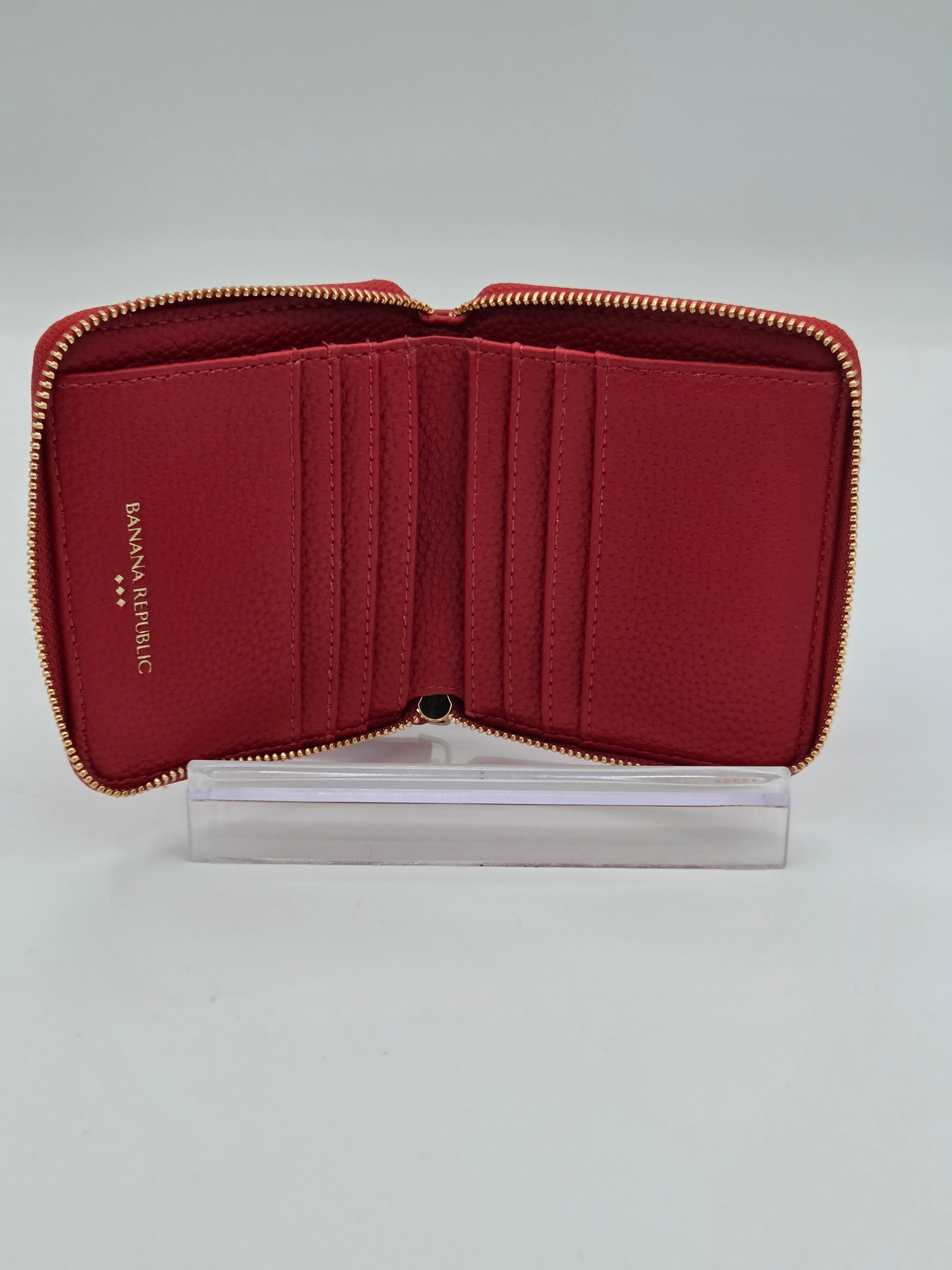 An open red leather zip-around wallet with multiple card slots and gold-tone zippers, displayed on a clear acrylic stand against a light gray background.